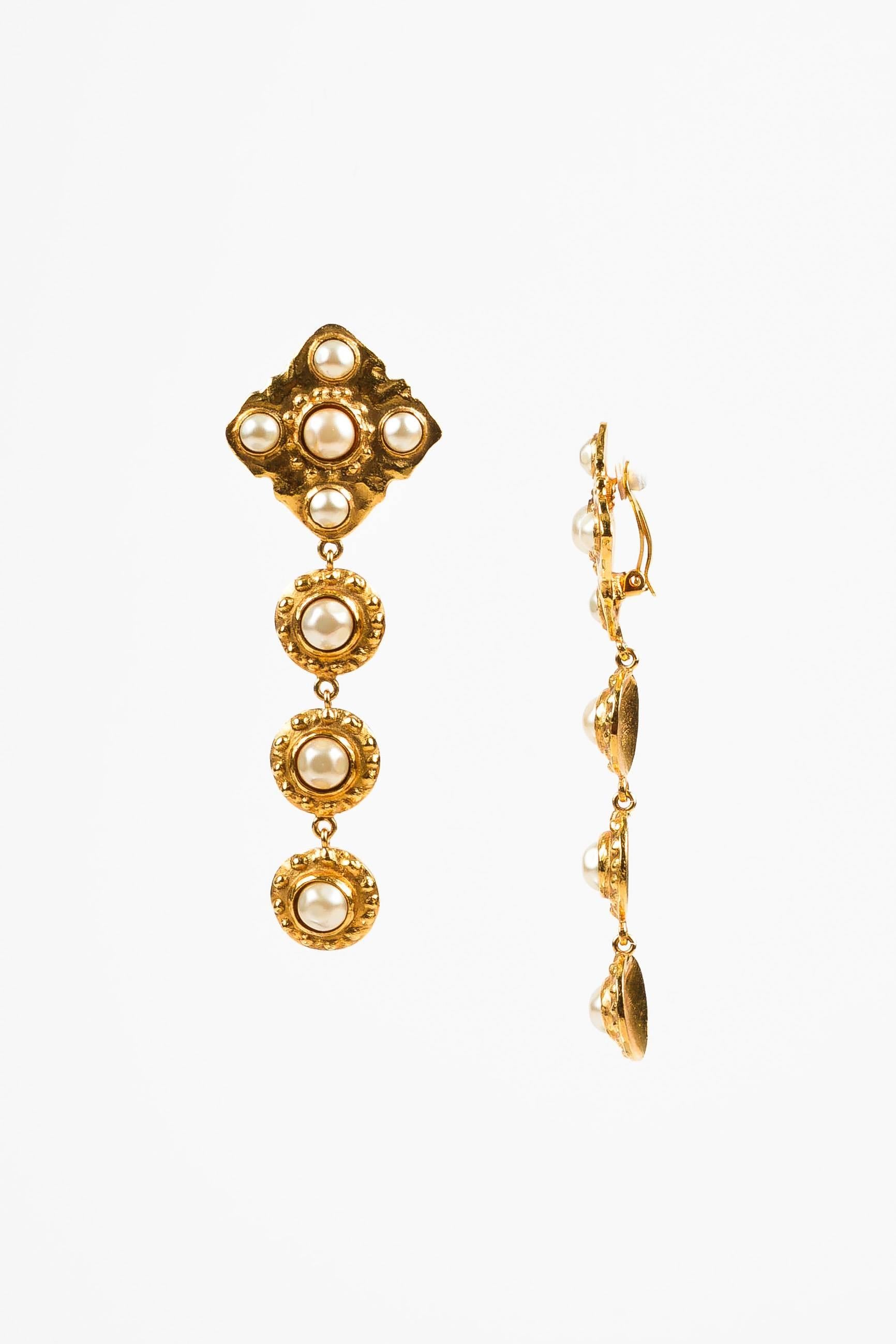Circa 1986, these vintage Chanel earrings feature dangling textured gold-tone metal discs. Each is embellished with a round faux pearl at the center. At the top is a square with matching texture and faux pearl detailing. Clip-on closure on back.