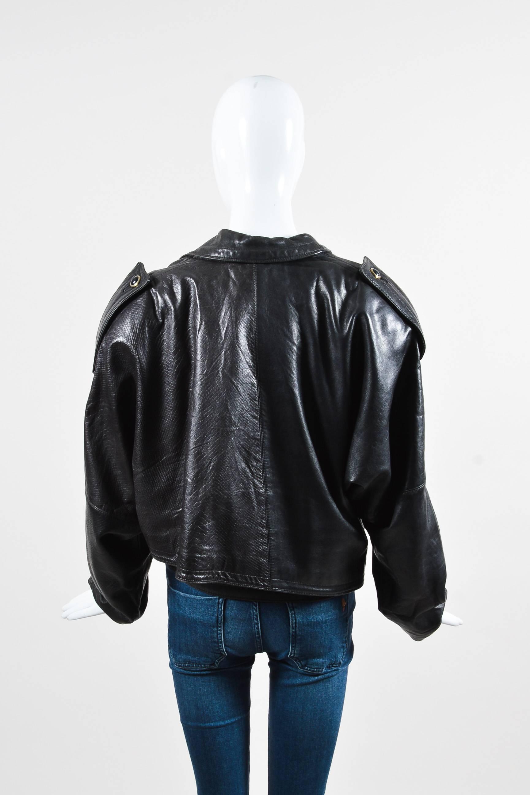 Vintage jacket featuring a cropped silhouette, structured shoulders, an asymmetrical lapel, buttoned tabs at the shoulders, a buttoned gun flap, and a single button-flap front pocket. Buckled strap at the waist. Embossed left side finishes off the