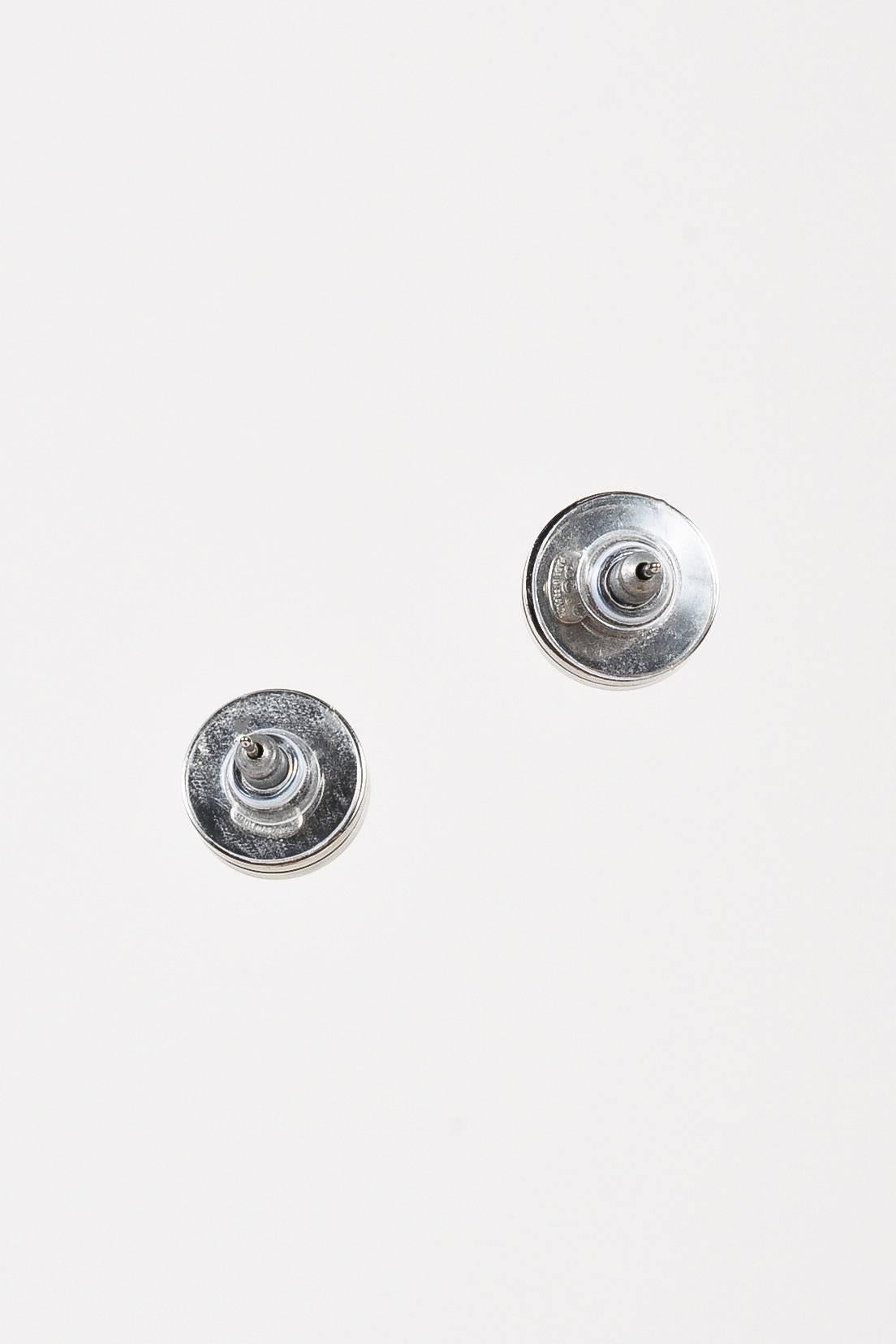 Simple and chic button earrings by Chanel from the 2003 Cruise Collection. Silver-tone metal settings featuring clear lucite over a reflective mirror topped off with white 'CC' logo embellishments. Post backs.

Measurements:
Additional