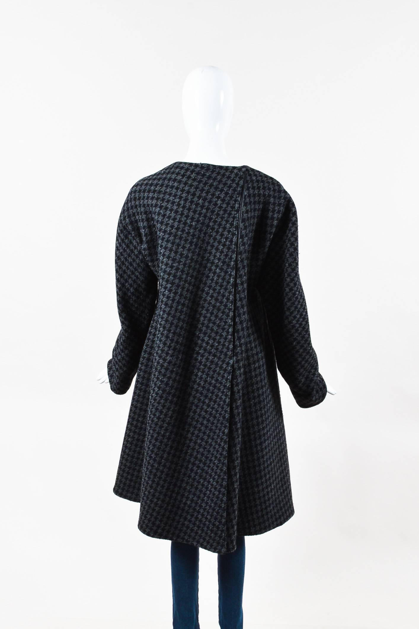 This oversized coat would pair well with a black leather pleated midi skirt and a white turtleneck. Black and gray houndstooth wool tweed coat from Gianfranco Ferre. Leather trim on the center front and back. Rounded neckline. Two buttons for