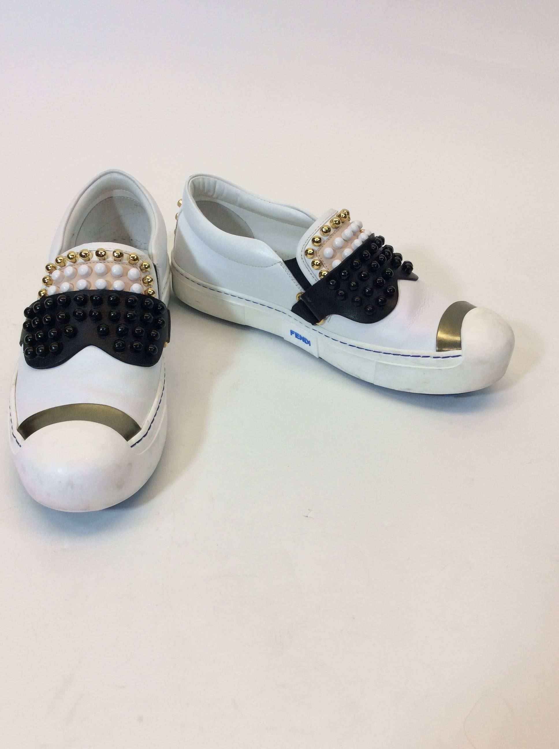 White and Black Fendi 'Karl' 
Studded Leather Sneakers 
Black, White and Goldstone Studs Along top and back
Slip-on shoes
Round toe with chrome Piece
Blue Pointed Sole 3.5" Inches 
'Karl loves Fendi' print
100% Calf Leather