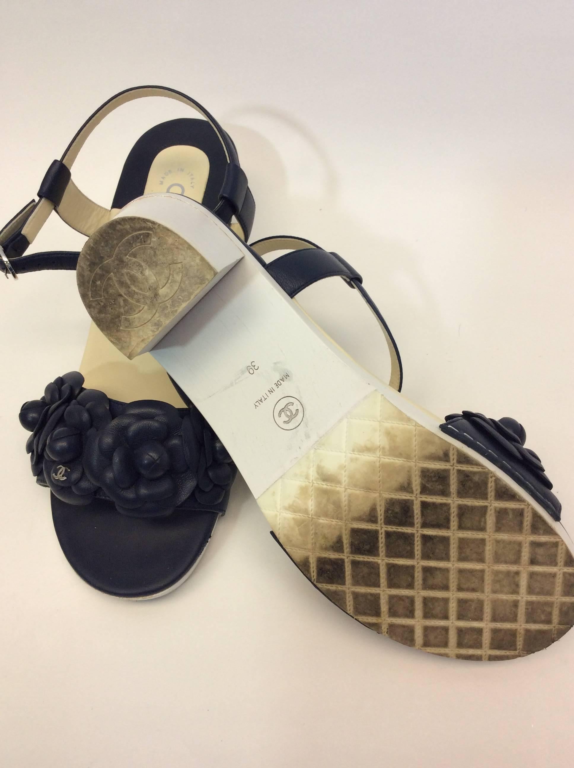 Navy Floral Strappy Sandal
2 inch heel
3.5 inch sole width
Adjustable buckled ankle strap
Chanel logo flower detail on toe strap
Size 39
Wood heel, leather upper and lining