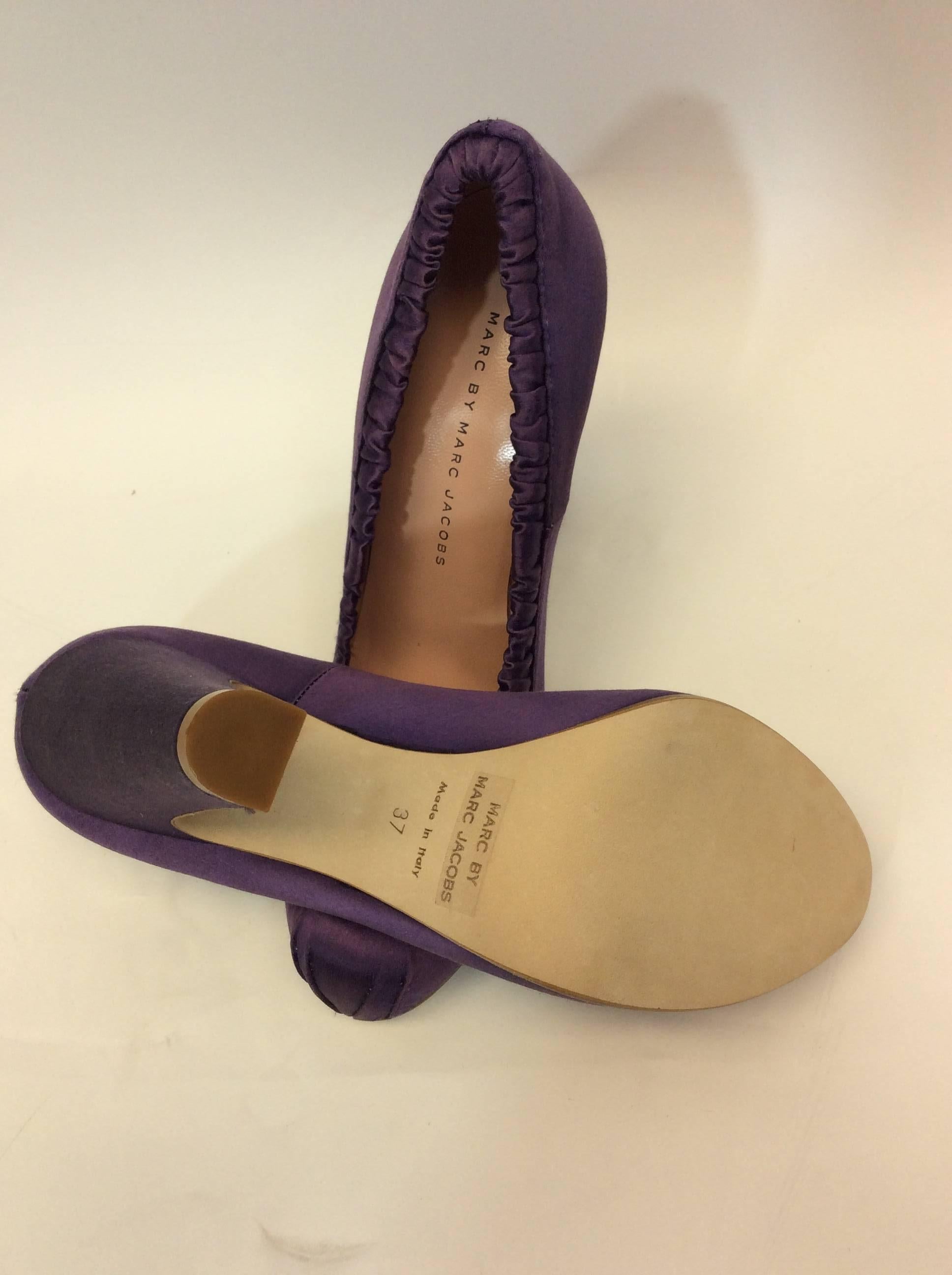 Purple Satin Pumps with Black Bow Detail
4.5 inch heel with 1 inch concealed platform
3.25 inch sole width
Elastic ruched detail around opening of pump
Black bow on toe of pump
Size 37
Satin upper, leather lining and sole
