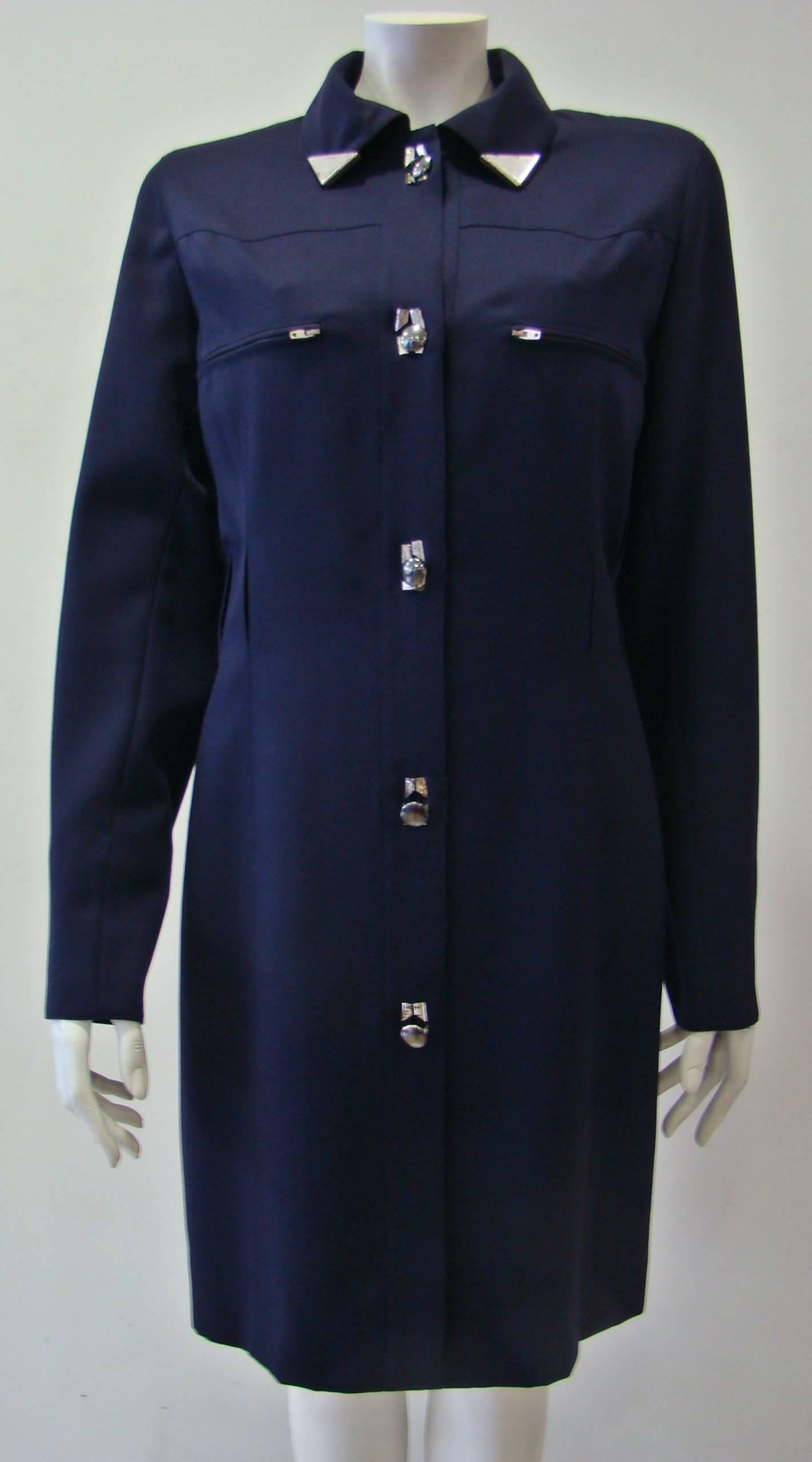 Crafted From Warm Wool This Claude Montana Navy Blue Dress Features Metal Tips In The Collar And Along The Front Buttoning. A Straight Line Dress With Two Zip Chest Pockets And Three Fuctional Buttons At Cuffs, Which Has Two Cut-Outs At The Waist So