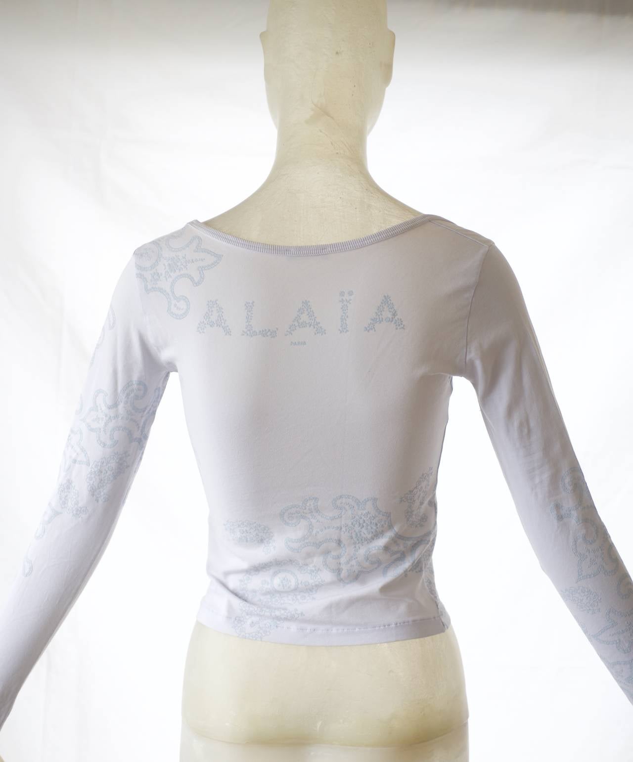 An Alaia strech shirt in a pale greyish blue with a paisley print and Alaia logo spelled out in tiny flowers on the back.  

Slips on.