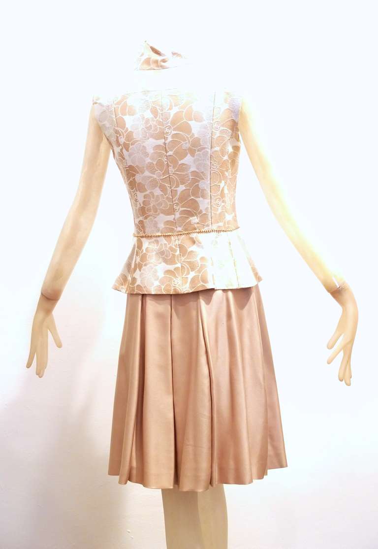 A pristine and most likely unworn Chanel cream and gold vest with a camellia pattern and silk camellia pattern lining vest.  Vest has an attached gilt and pearl belt and pearl toggle zipper with tiny CC adorning the pearl.  Matching silk skirt.
