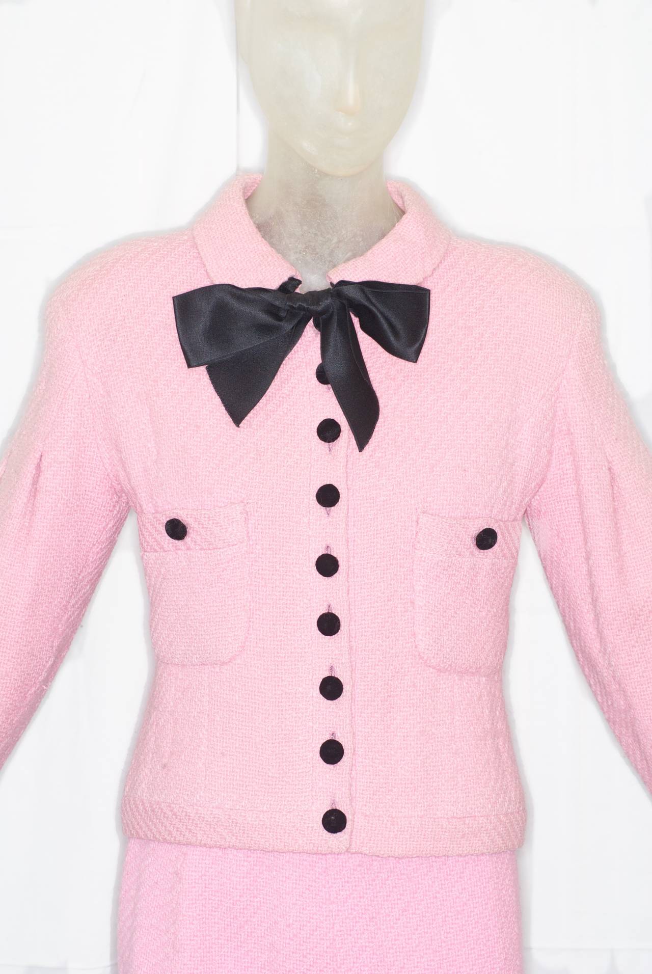 A pink Chanel haute couture suit with black silk bow from the 1990s.  Buttons and cuffs are black silk velvet.  Lining is quilted pink silk with gilt chain running along hem.  Black silk velvet kick pleat detail on front of skirt.

jacket:
total