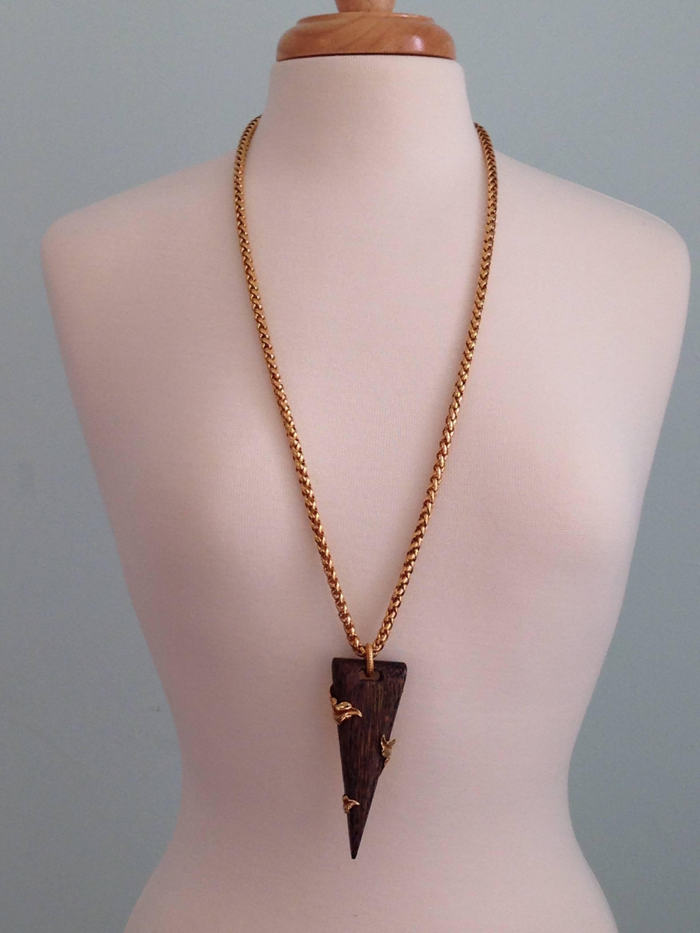 Amazing statement necklace from Dominique Aurientis featuring a long 34" gold tone chain and a faux wood pendant accented with gold leaves measuring  4" long and 1 1/2" wide. The necklace is signed on the back with a round plaque