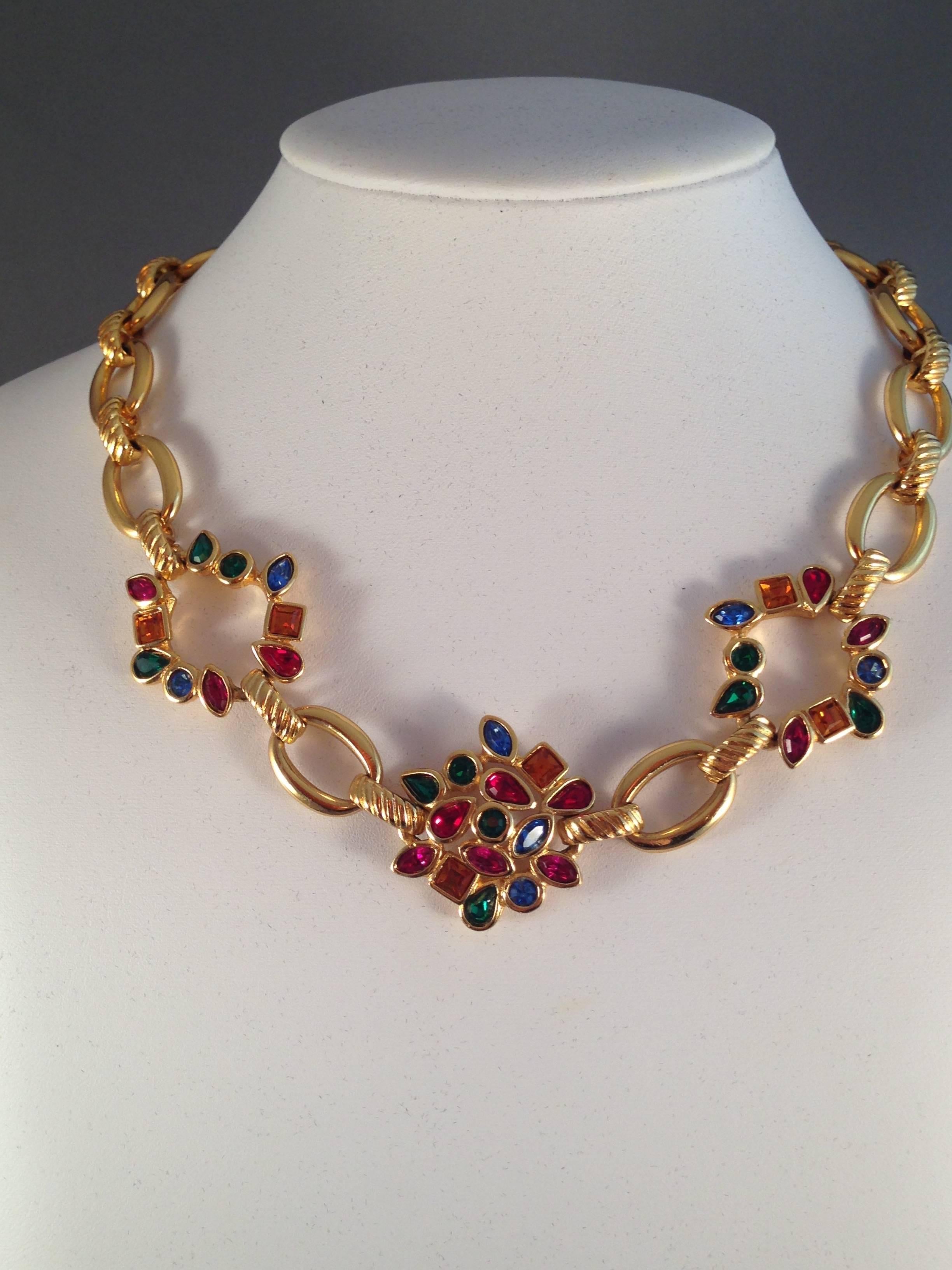 This is a 1980s Yves Saint Laurent gold-tone necklace set with beautiful, sparkling, multi-colored glass stones. It measures 17" long and 1 1/4" at its widest point. The necklace closes with a clasp that is marked 'YSL Made in France' on