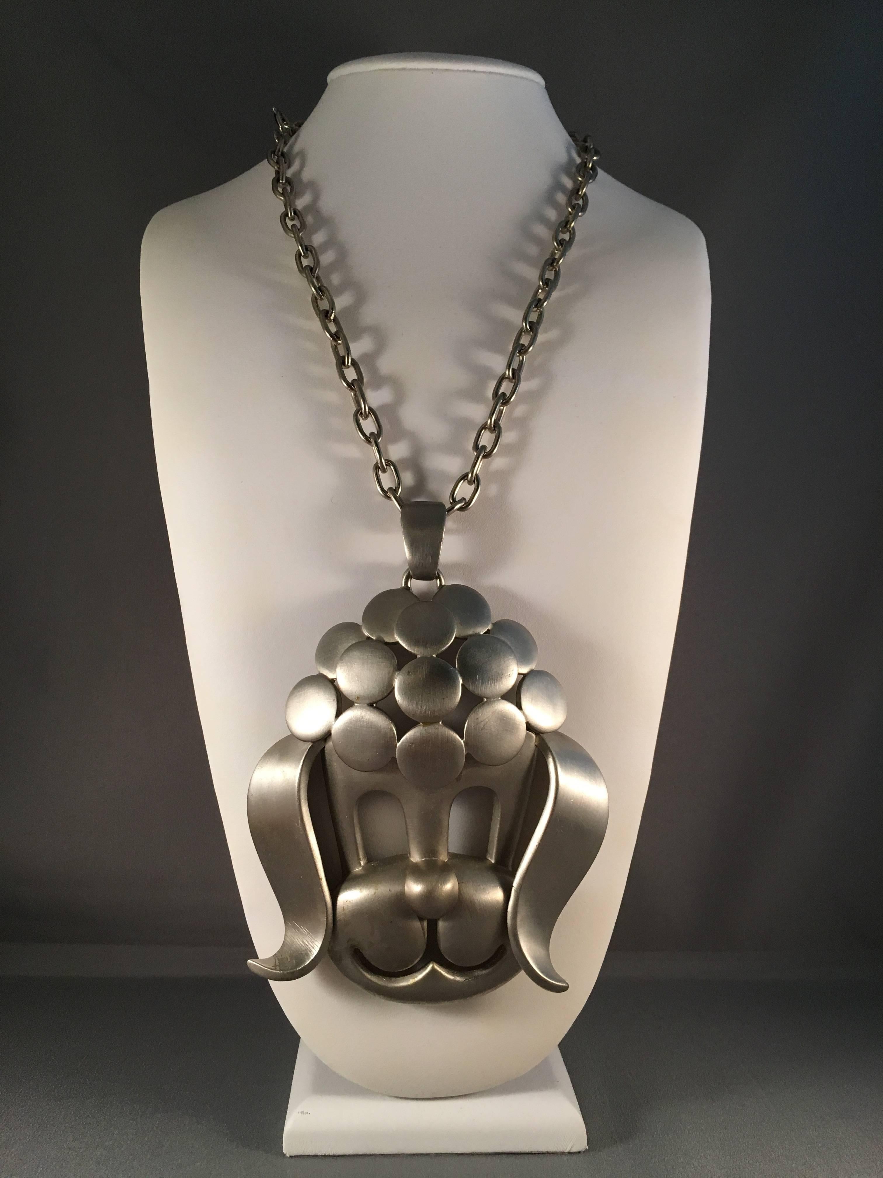 This is an amazing Pierre Cardin statement necklace from the 1960s. It features  a huge mod poodle pendant measuring 5 1/4" long x 4 3/8" wide on a 21" long silvertone chain. Image #3 shows the pendant in comparison to a quarter so