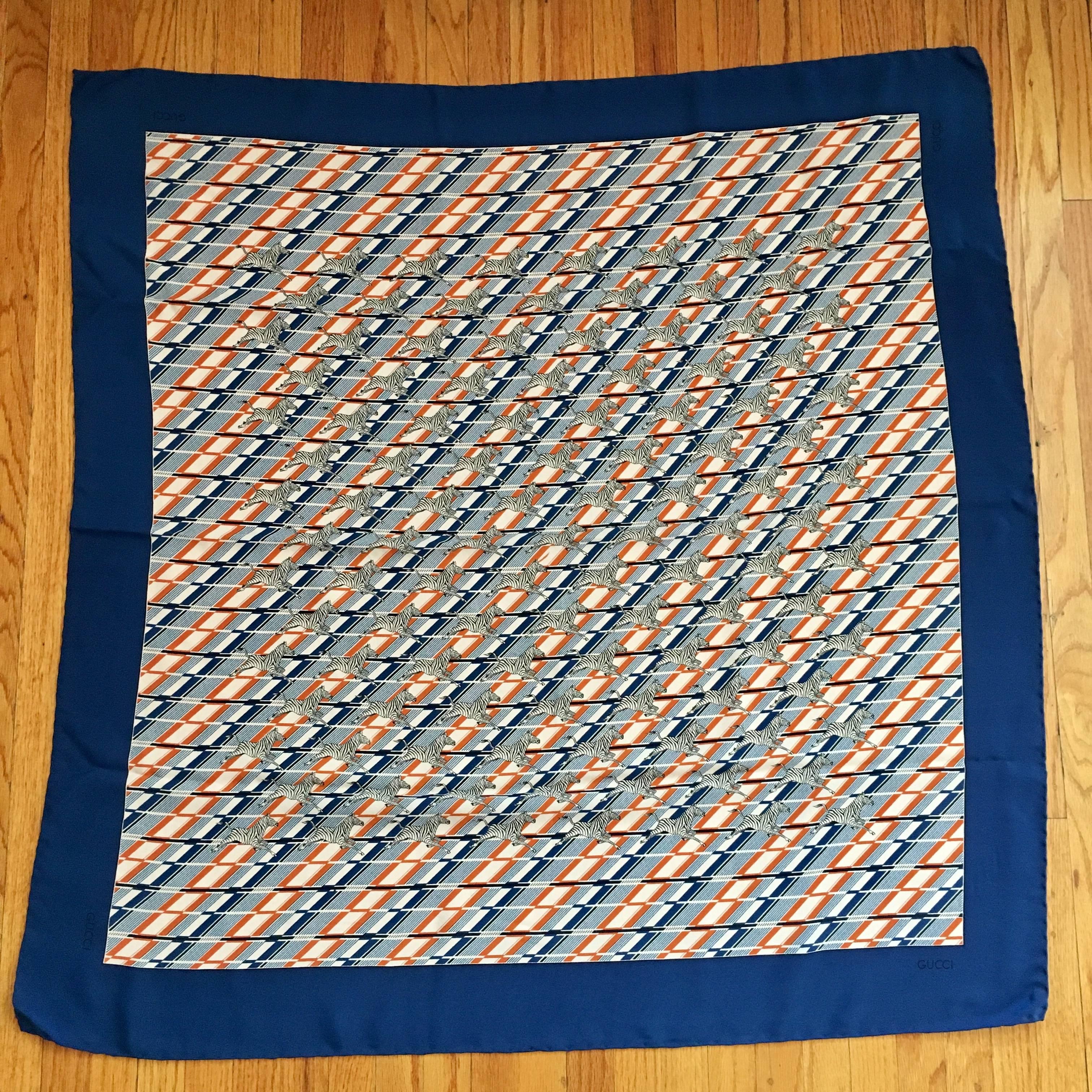 This is a fabulous 1970s scarf from Gucci featuring zebras running over a geometric background of navy, white and orange. It is 100% silk. The edges are hand-rolled and stitched. Each corner is marked Gucci. There is a tag that reads '100% silk Made
