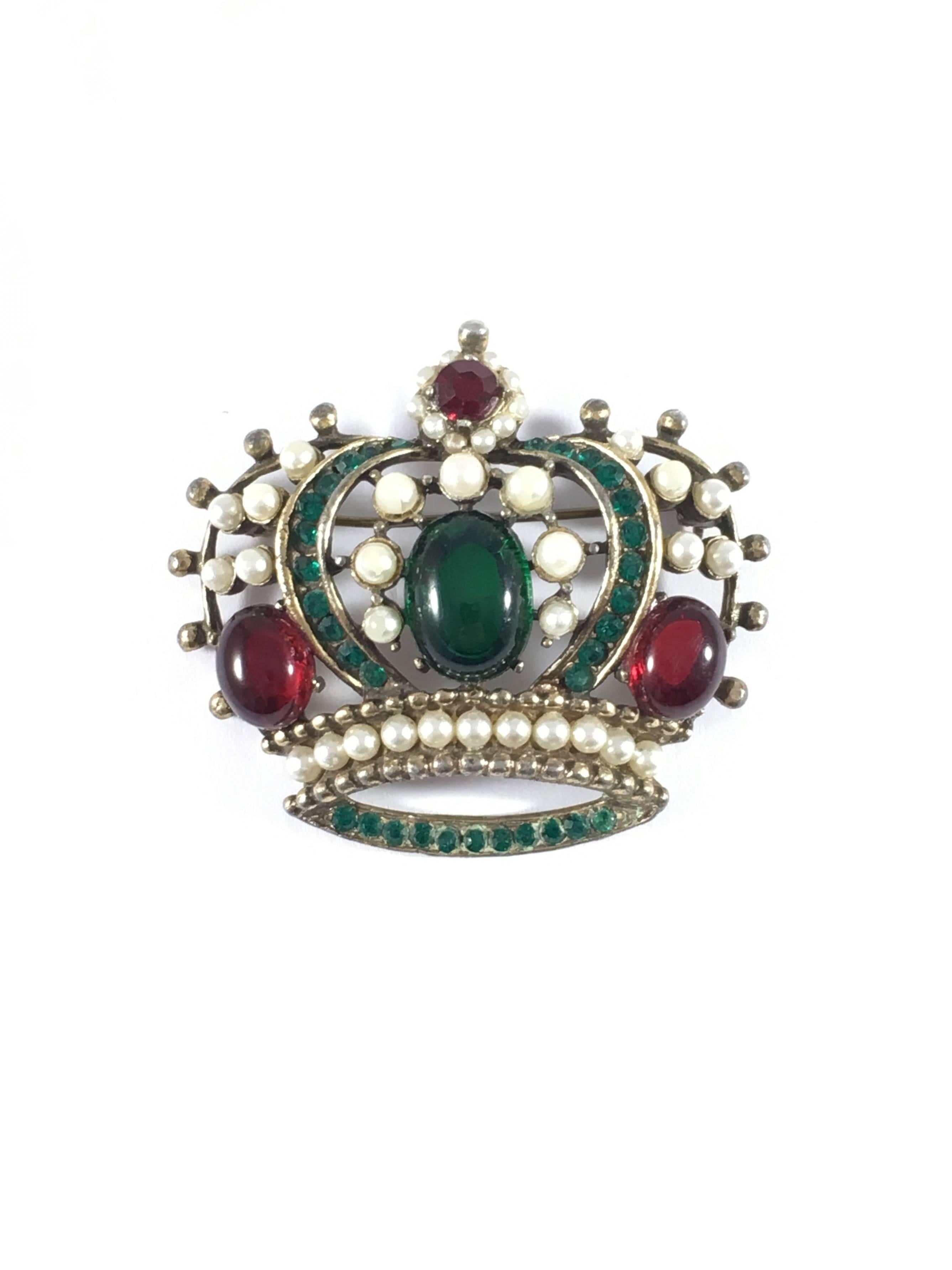 This is a 1950s Weiss crown brooch pendant made out of a gold-toned metal embellished with red and green glass stones, rhinestones and faux pearls. The brooch measures 2 inches wide x 1 3/4 inches high. It is marked 'Weiss' on a plaque located on