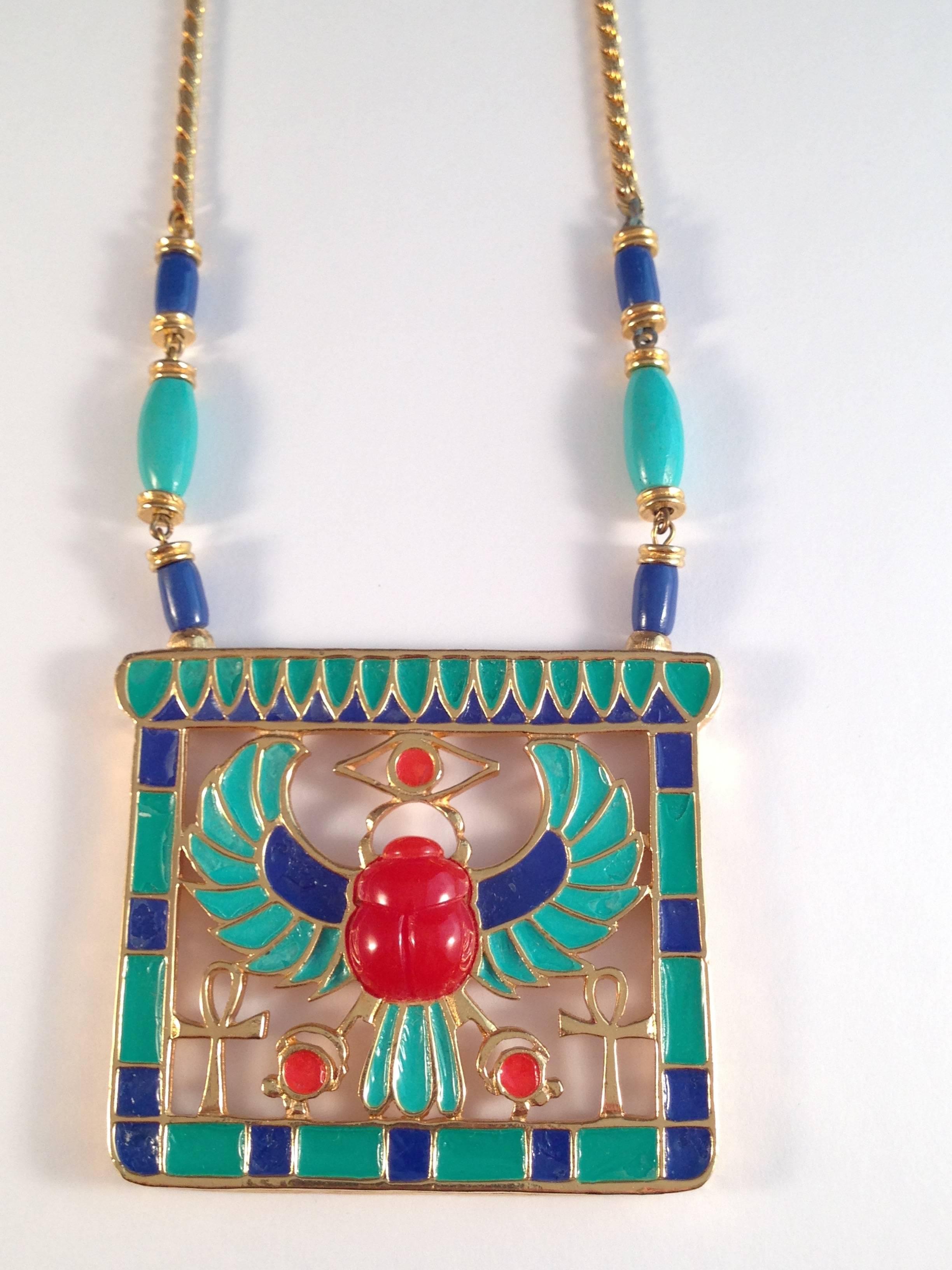 This hard to find Egyptian revival pendant necklace was made in the 1960s by Hattie Carnegie. It features an enameled gold tone pendant in brilliant blue and turquoise with a resin amber-colored winged scarab in the center. The chain measures