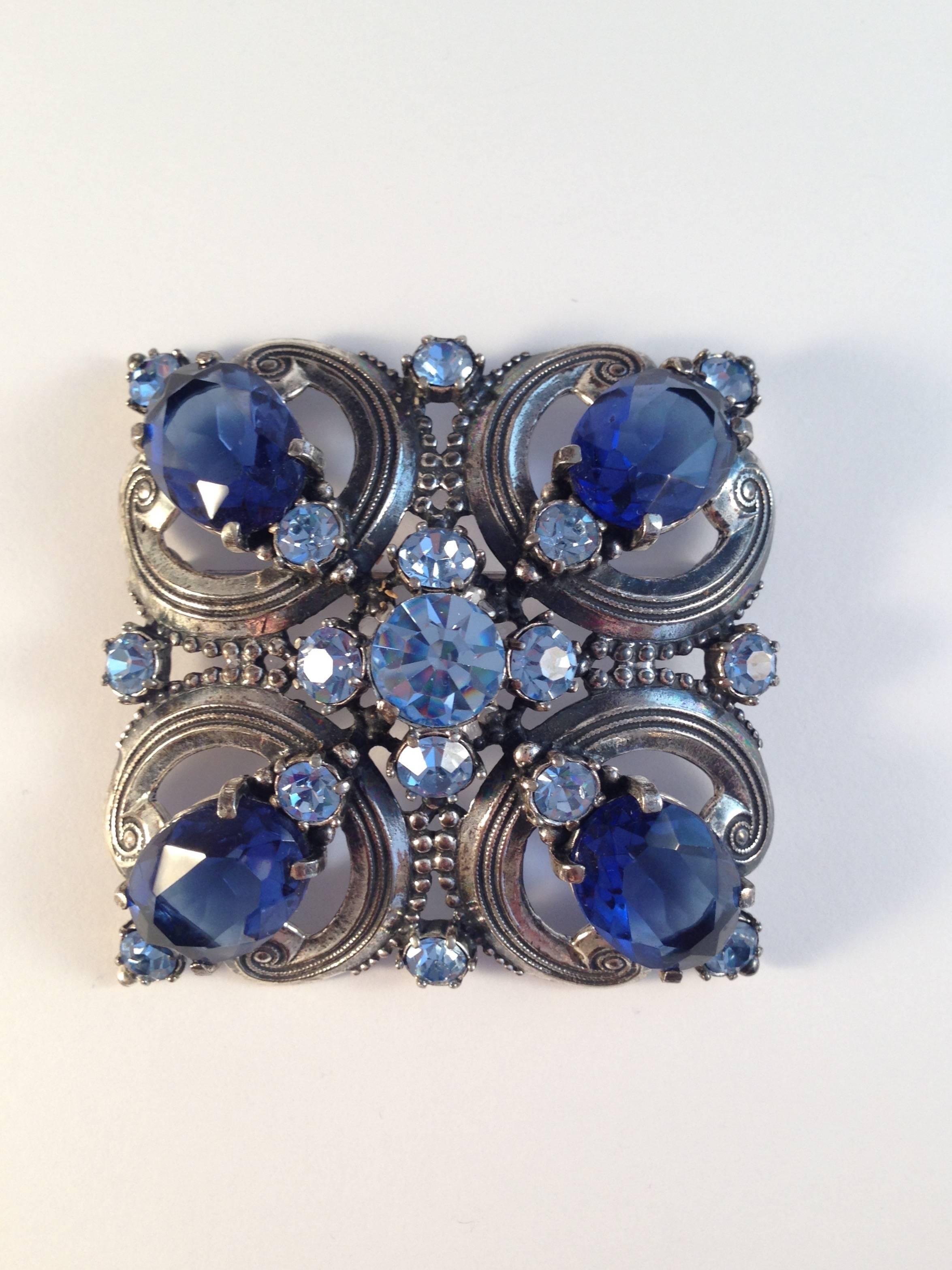 This is a beautiful blue and silver-tone 1940s Elsa Schiaparelli brooch and clip-on earrings set. The brooch measures 2 3/8" x 2 3/8". It is silver-tone metal set with beautiful sapphire blue and light blue glass stones. It is in very good