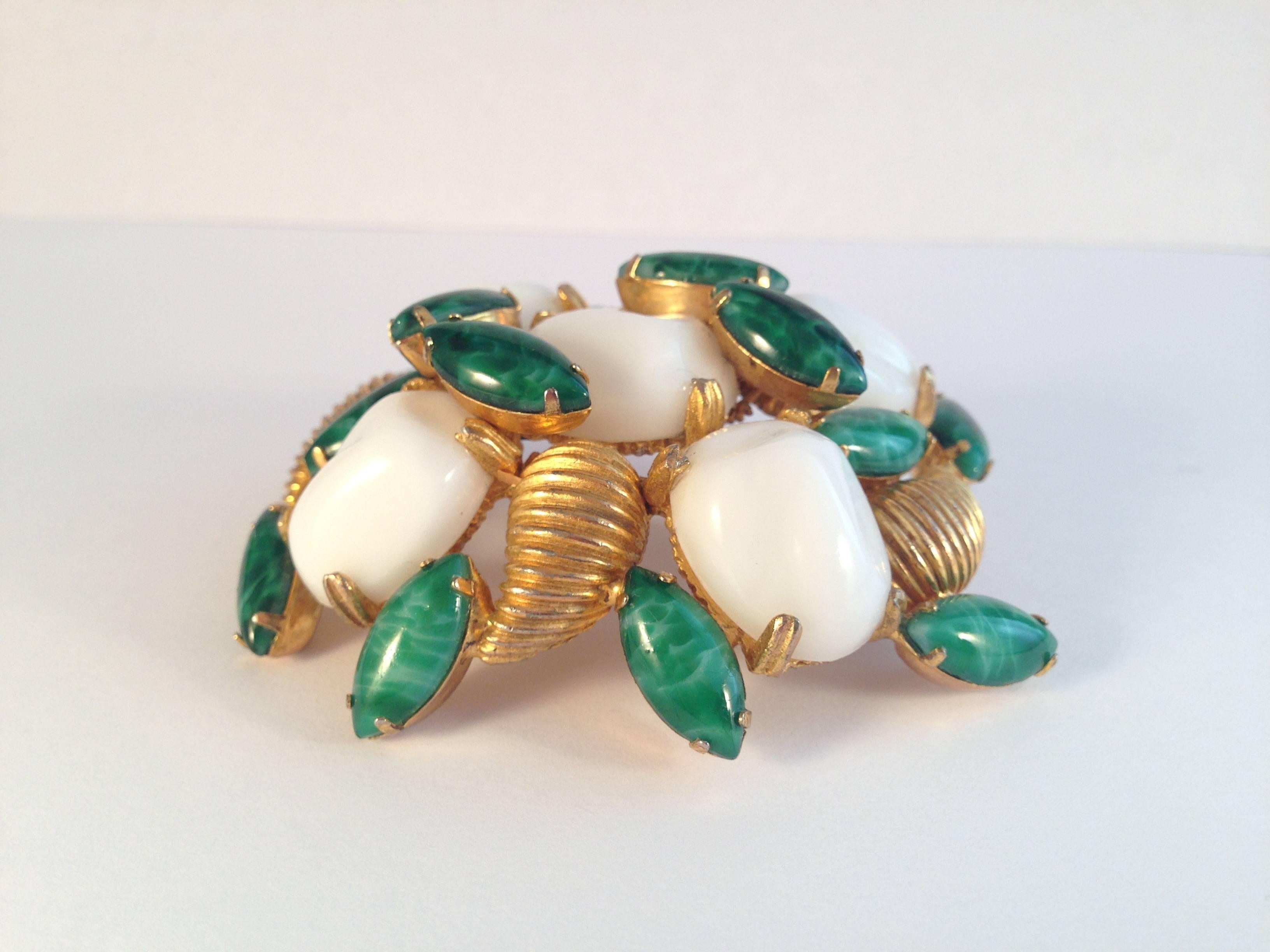 This is a 1960s Mimi di N gold tone brooch set with white and green glass cabochons. It is large and measures 2 1/2" wide x 2 1/8" high. It is marked 'Mimi di N' in an oval plaque on the back of the brooch. It is in excellent vintage