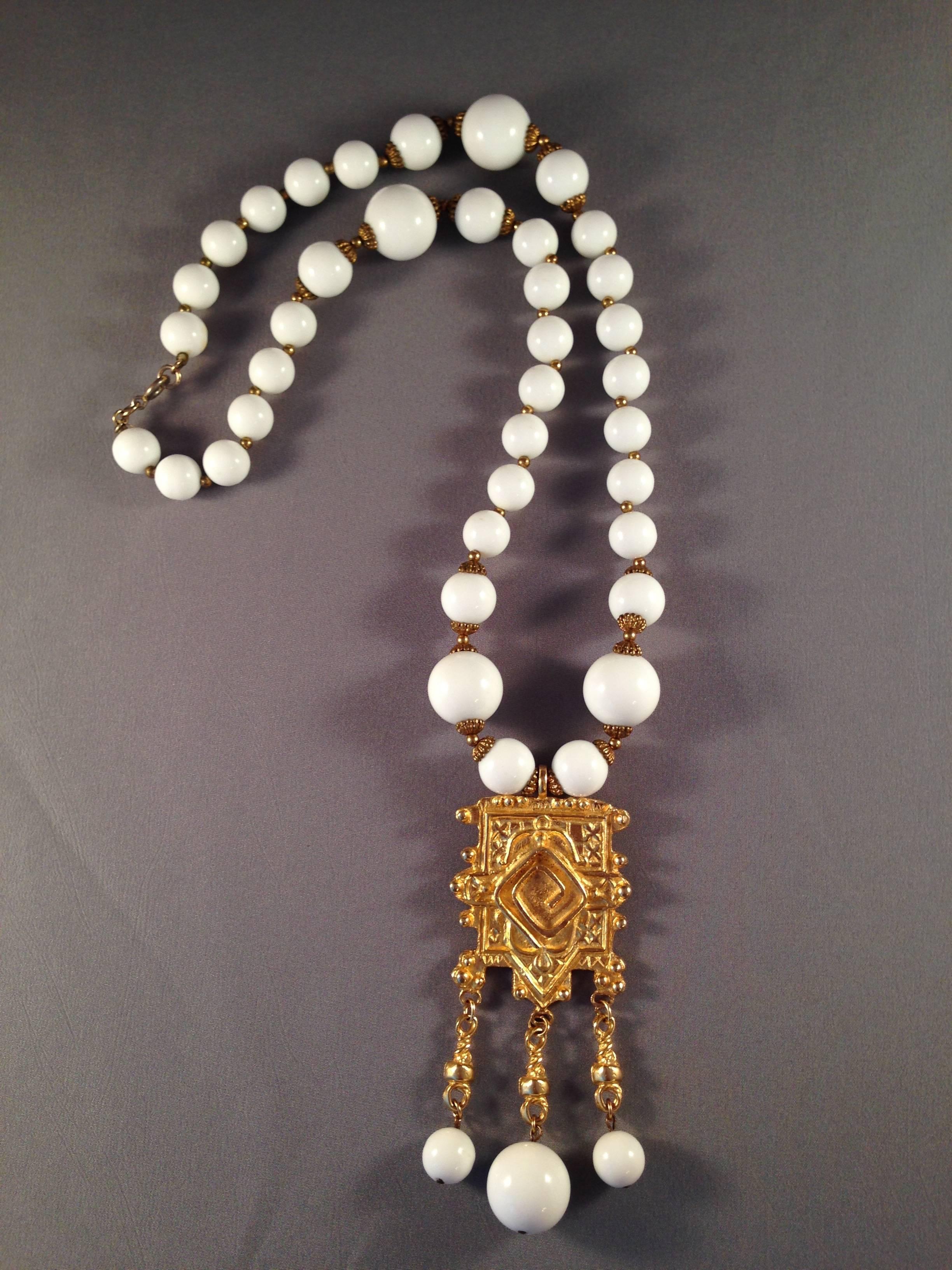 This is a 1960s white bead necklace with a gold pendant from Cadoro. The necklace is 24