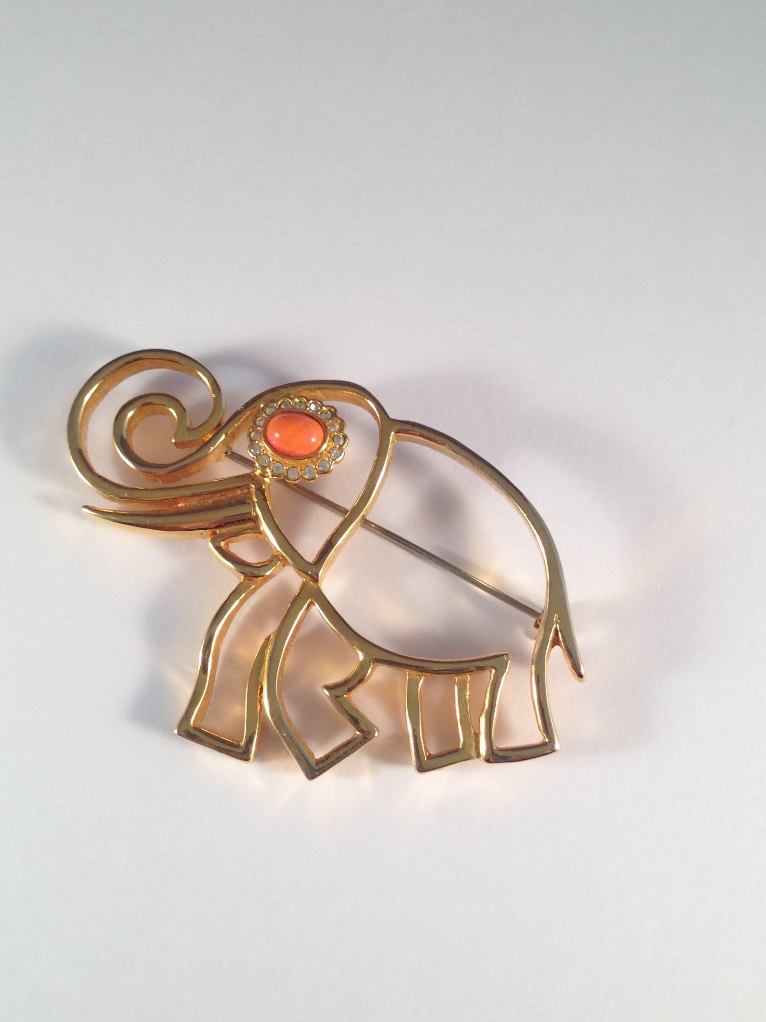 This is a 1960s gold tone elephant brooch from Kenneth Jay Lane. It has a coral colored glass stone for an eye surrounded by clear rhinestones. It is marked 'K.J.L.' on the back - the signature Lane used in the 1960s. The brooch measures 3