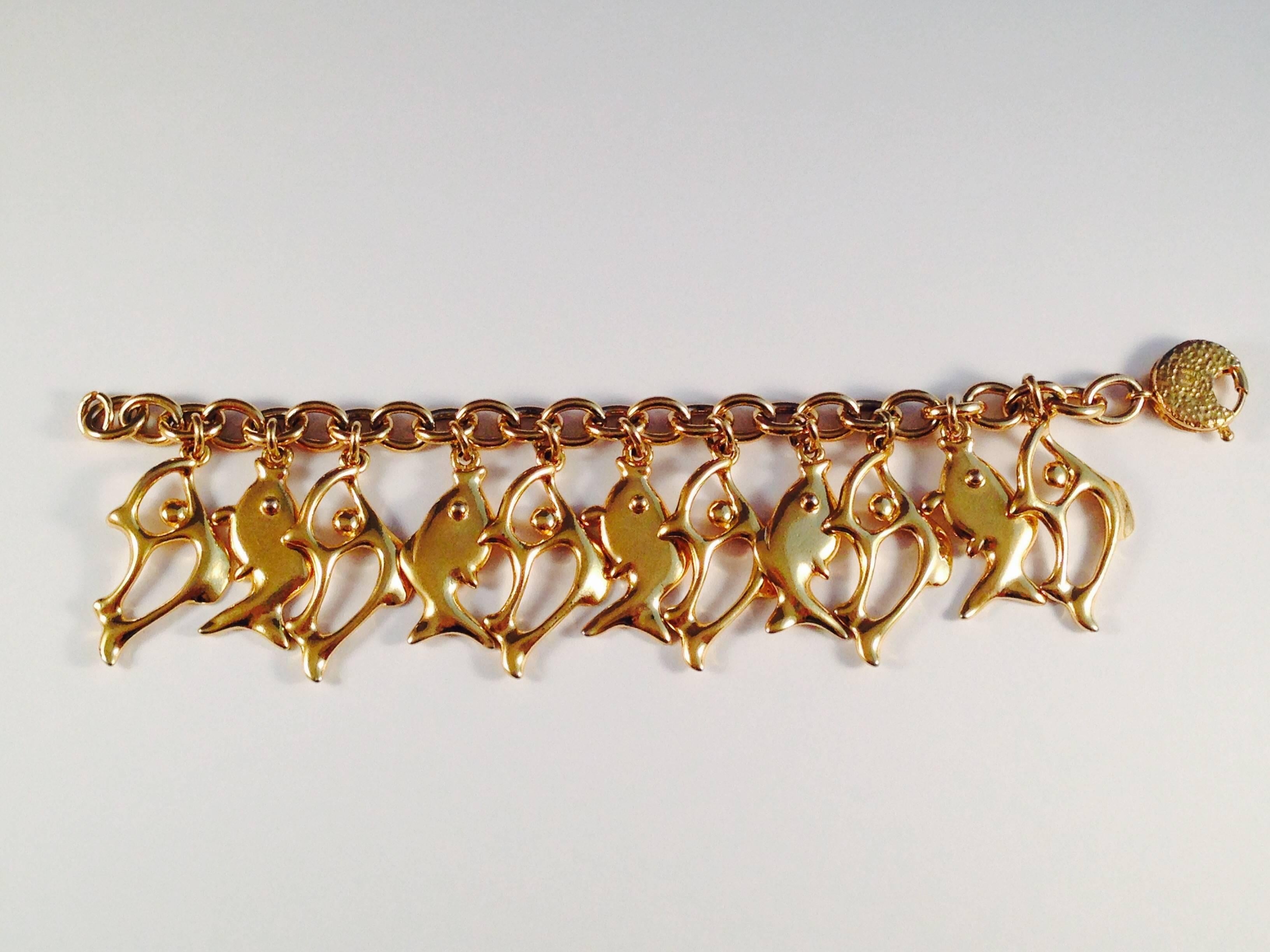 This is a gold tone Yves Saint Laurent fish charm bracelet from the 1980s. It features 1 3/4