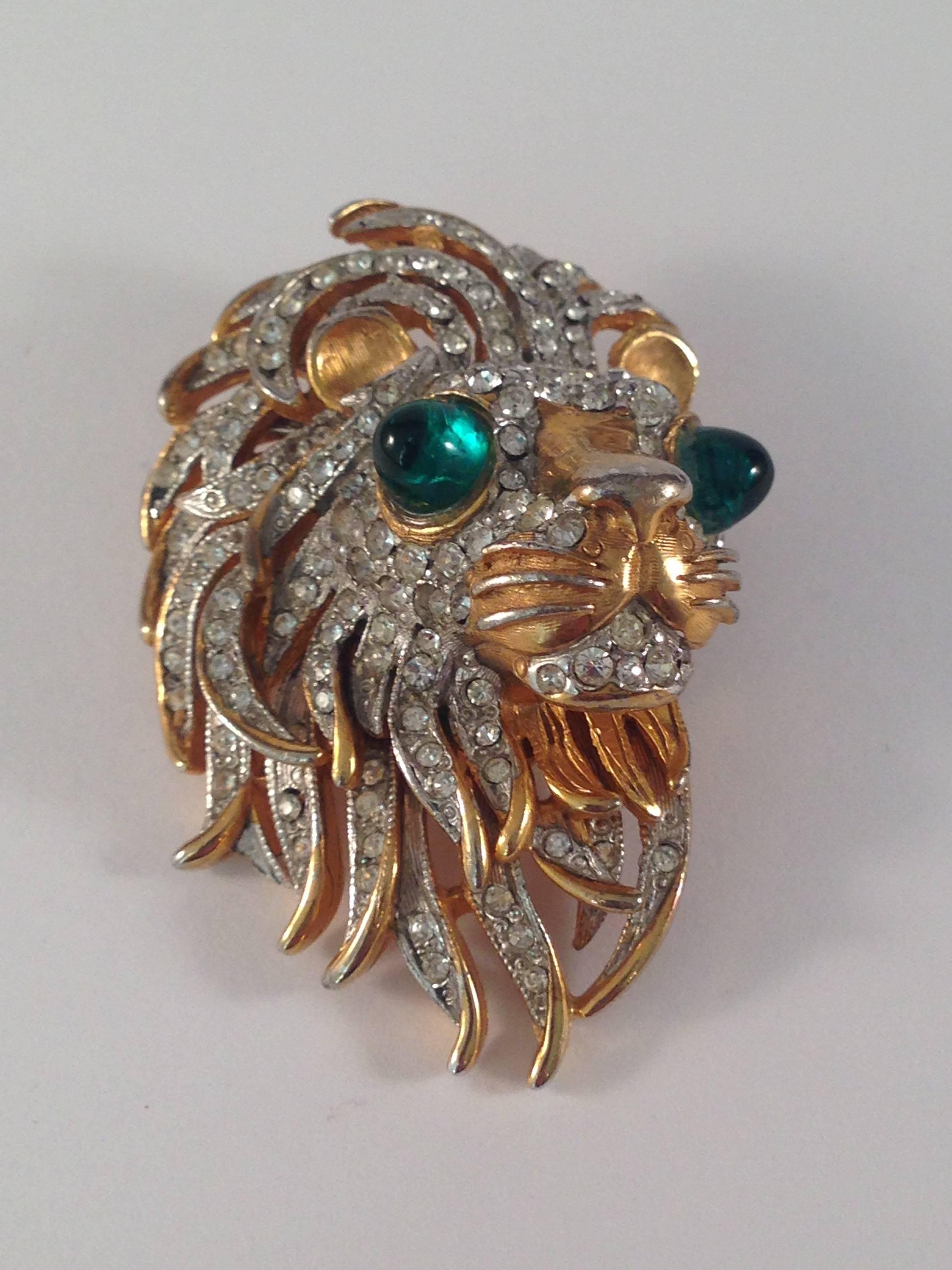This is a 1960s Kenneth Jay Lane lion or Leo head brooch. It is gold tone metal with clear rhinestones and green glass eyes. It is marked 'K.J.L.' on the back - the signature Lane used in the 1960s. It is in very good vintage condition with slight