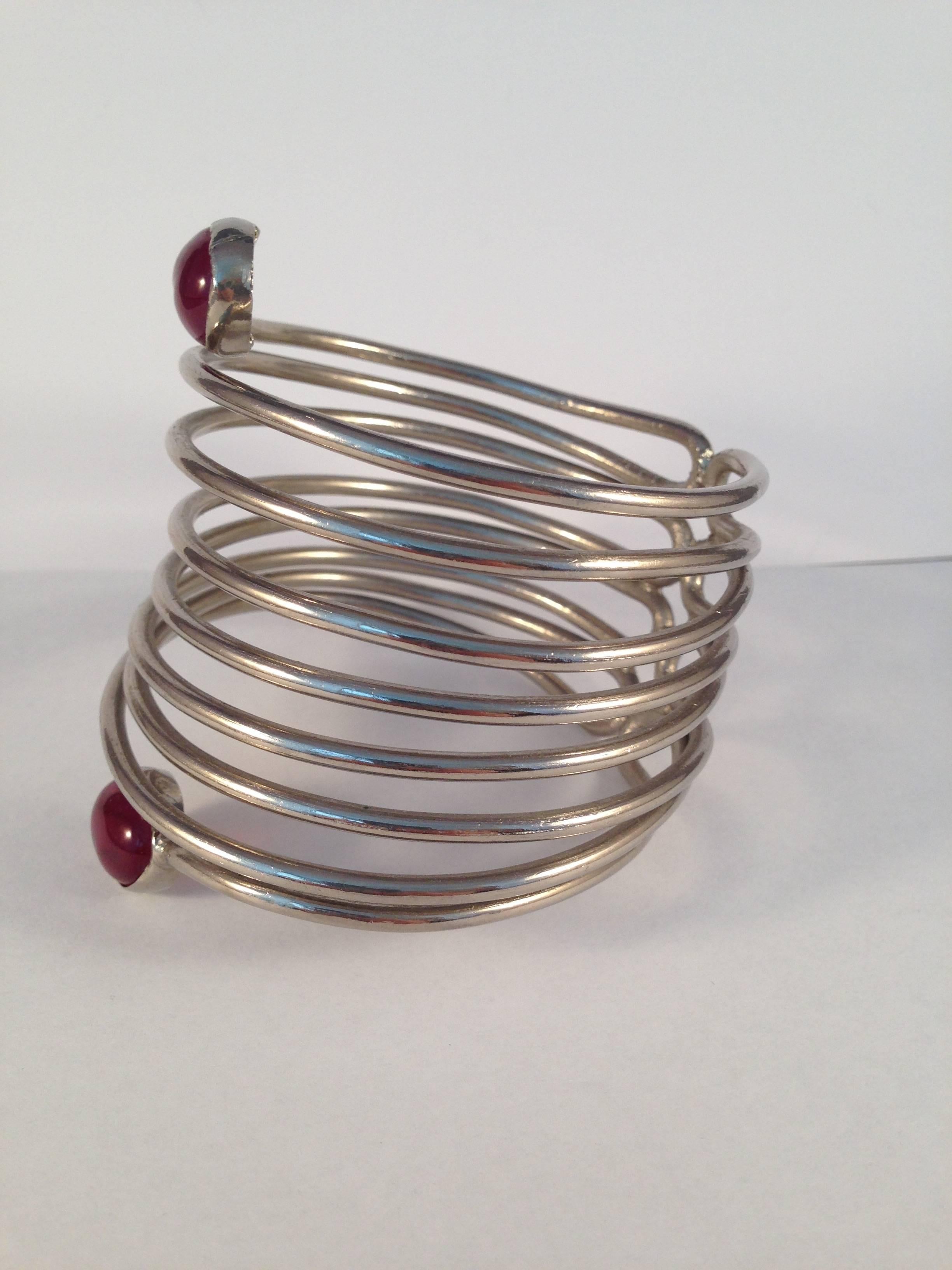 This unique 1970s Yves Saint Laurent silver-tone spiral cuff bracelet is a stunner and measures 3" tall. It features a spiral design with hand poured red gripoix glass at each end. The diameter of the bracelet is 2 3/4". It is marked