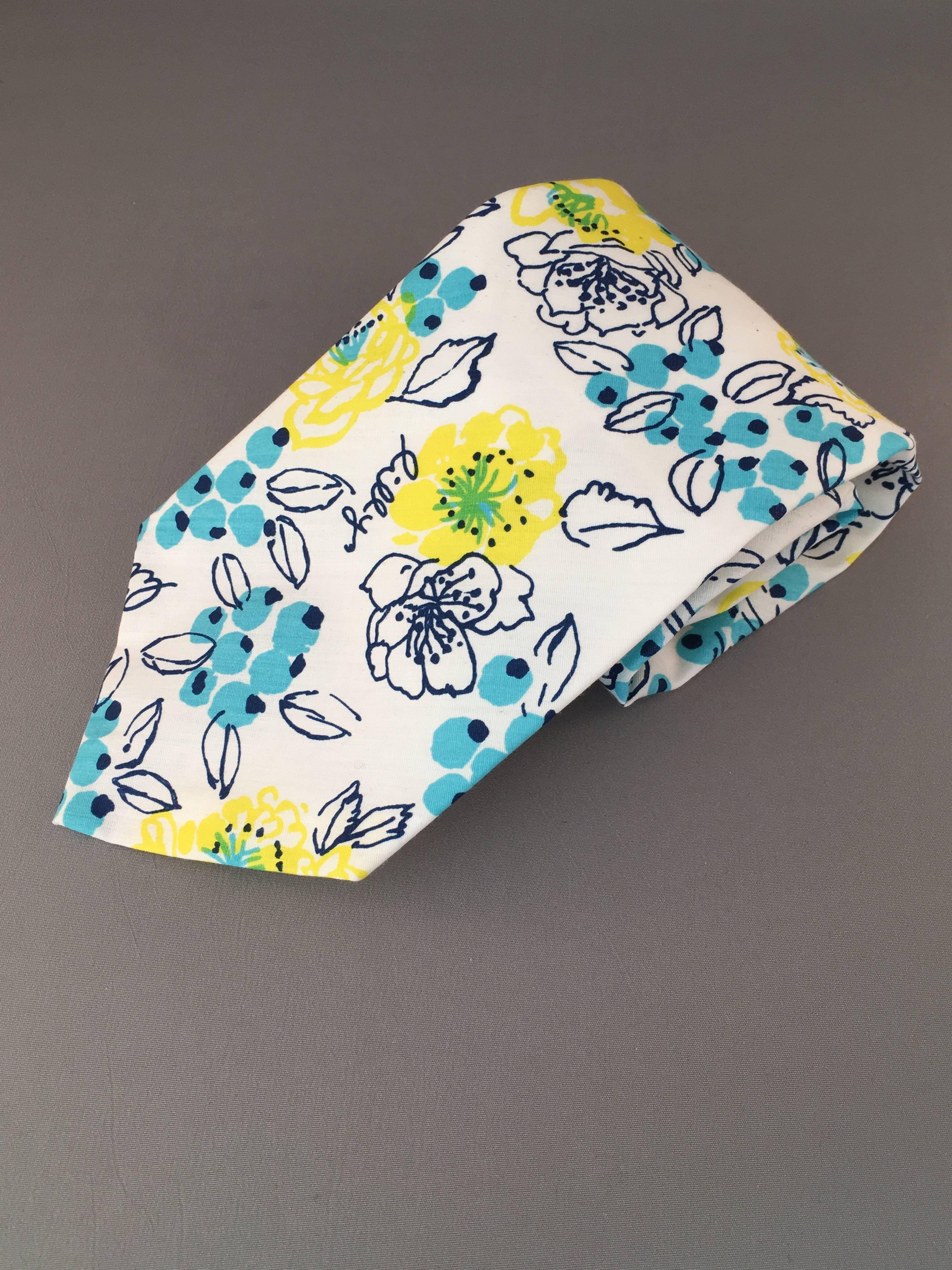 This is a classic 1970s printed Lilly Pulitzer 'Mens Stuff' tie. It features a blue and yellow floral print on a white background. In true 1970s style, it is very wide. It measures 4" at its widest point. The tie is in excellent condition and