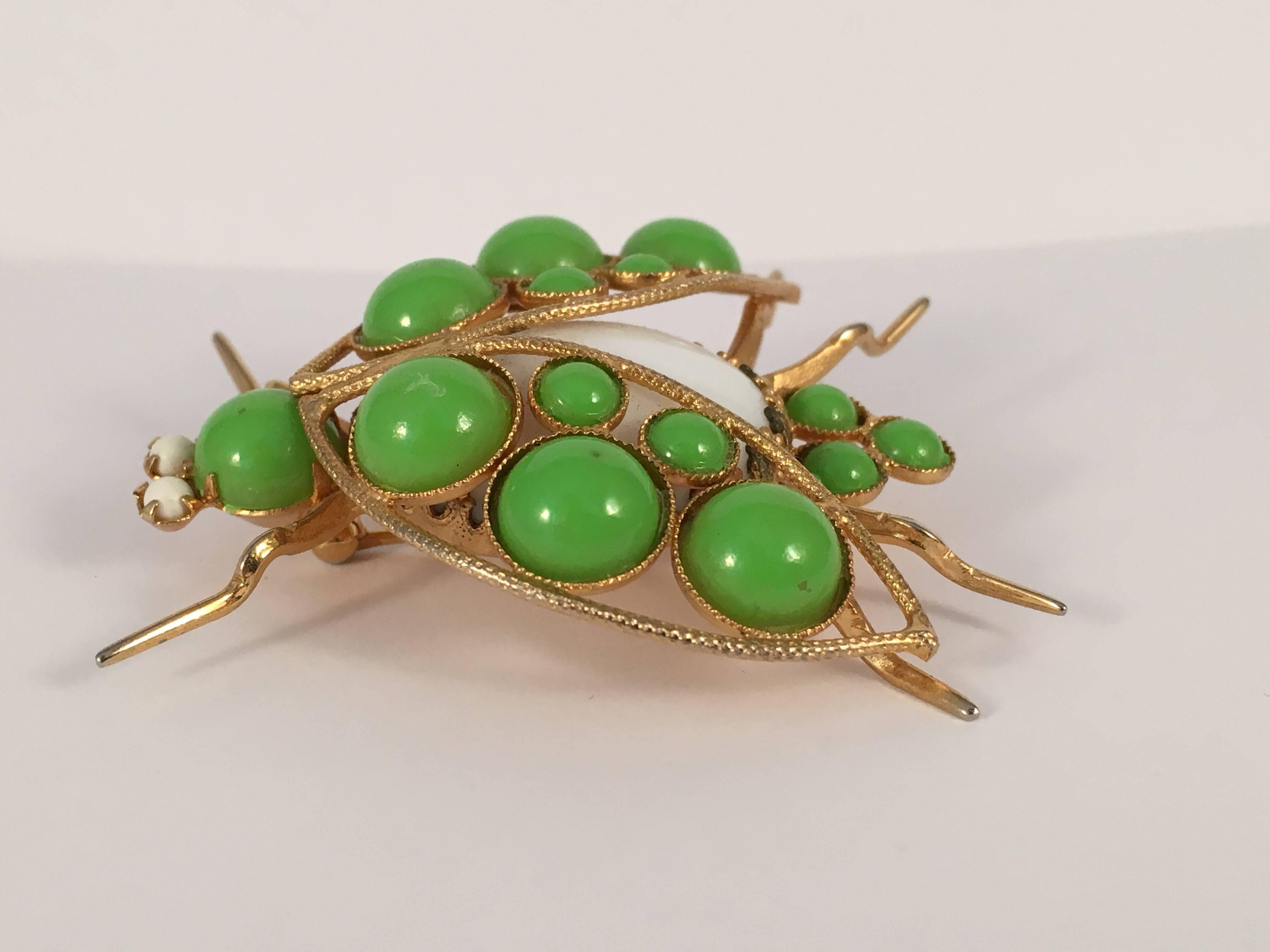 This is a green Kenneth Jay Lane bug brooch from the 1960s. The bug's body is made out of a white glass stone. The head and wings are made out of green resin beads. It measure 2 1/8