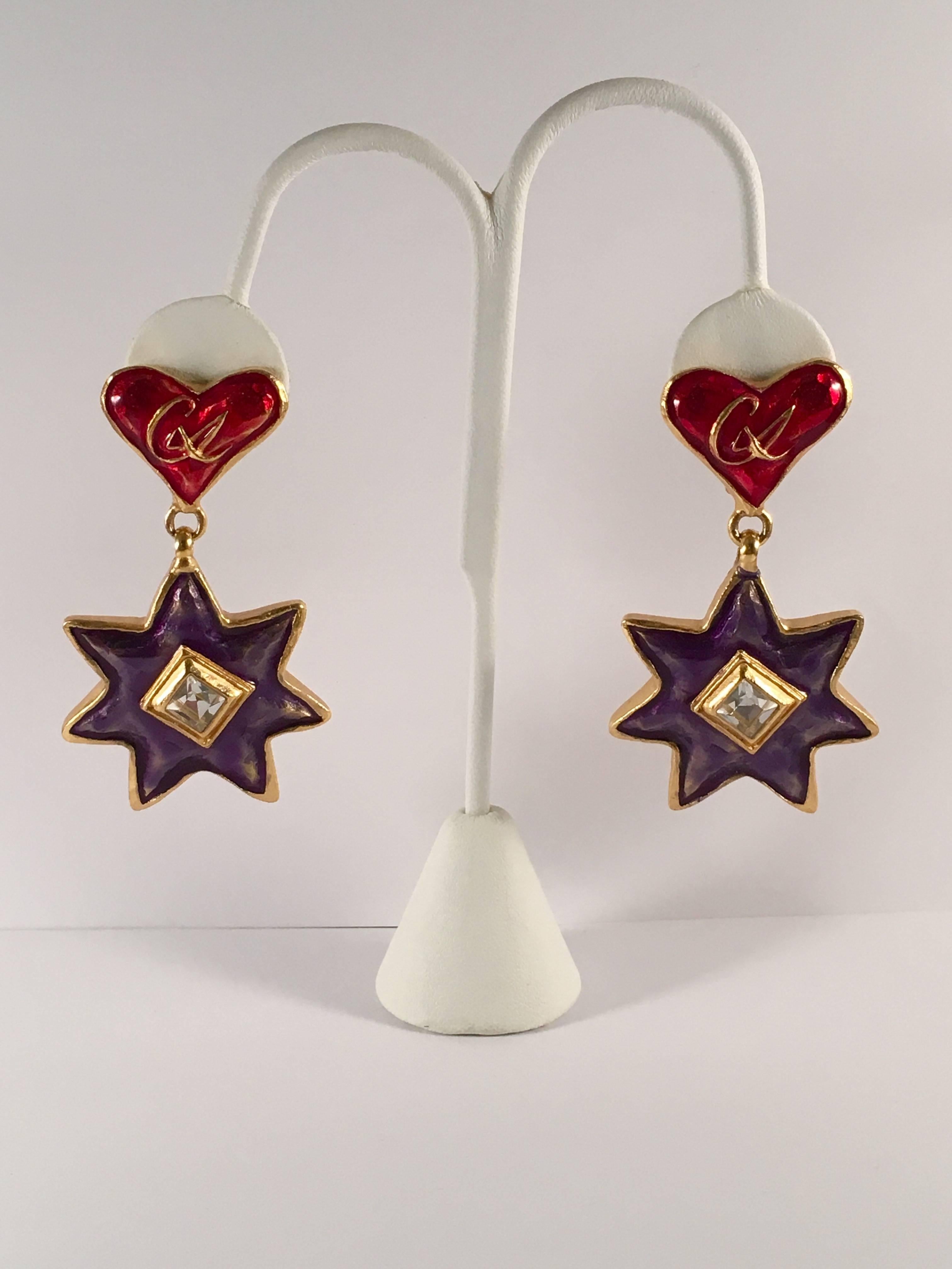 This is a pair of Christian LaCroix clip-on dangle earrings from the 1990s. The clip portion features an enameled red heart with a gold "CL" in the center. The dangle portion features a blue enameled star with a shiny clear rhinestone in