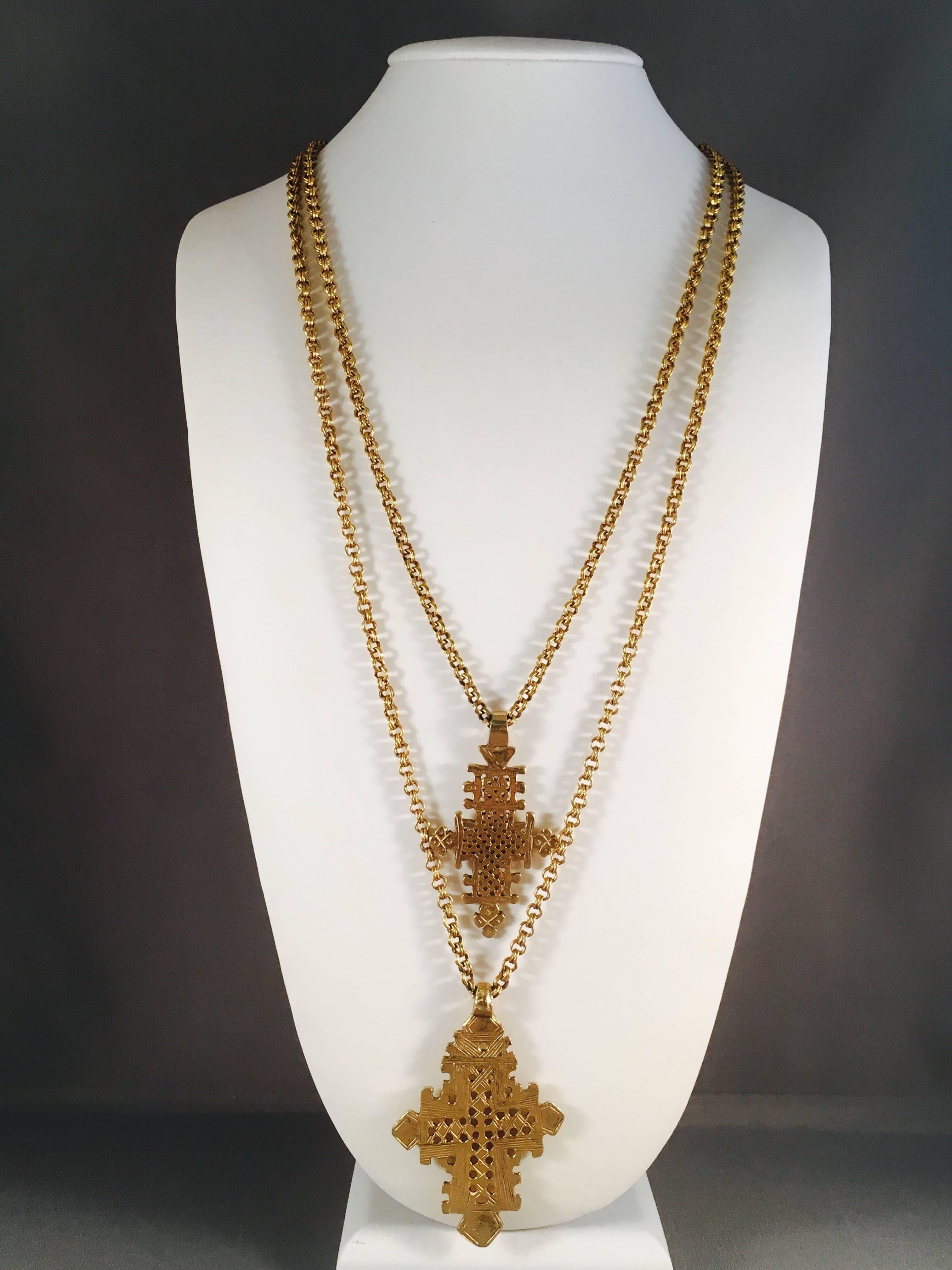 This is an incredible 1970s gold-toned double strand necklace from Accessocraft. It has two cross charms. The shorter necklace strand measures 25" long and the longer chain measures 30" long. The smaller cross charm measures 2 1/2"