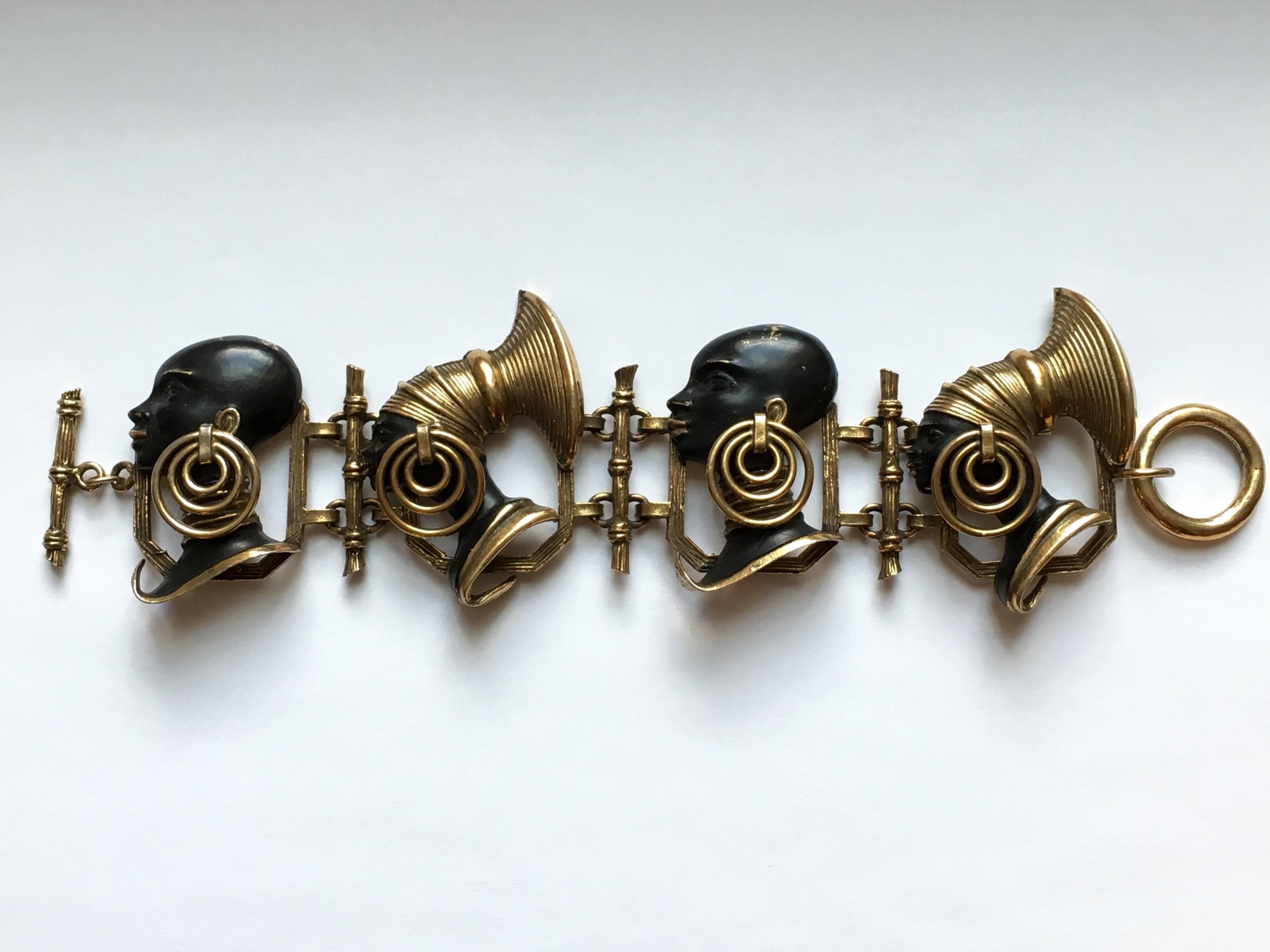 Rare 1940s beautifully made, brass, enameled bracelet and earring set made up of the heads of African men and women wearing tribal earrings, necklaces and head gear. The earrings that the figures are wearing, hang down and actually move a little