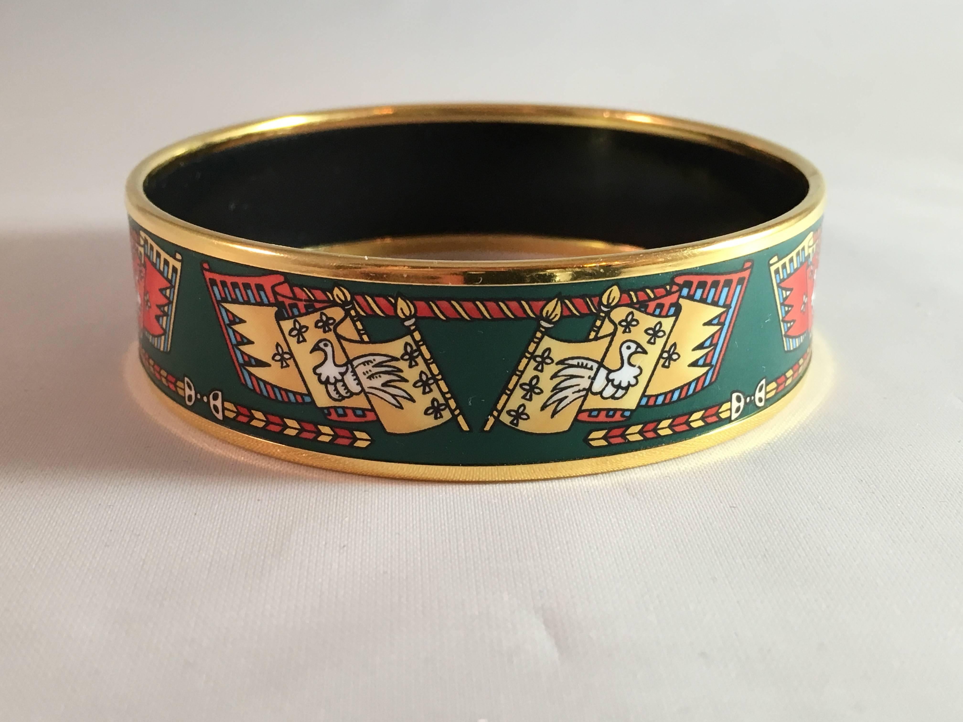 This is a great vintage printed enamel Hermes bracelet. It has a green ground with printed flags in red and gold. It is measures 7/8" wide and has an opening of 2 3/4" or 70mm. The interior is signed with a caleche coach and the words
