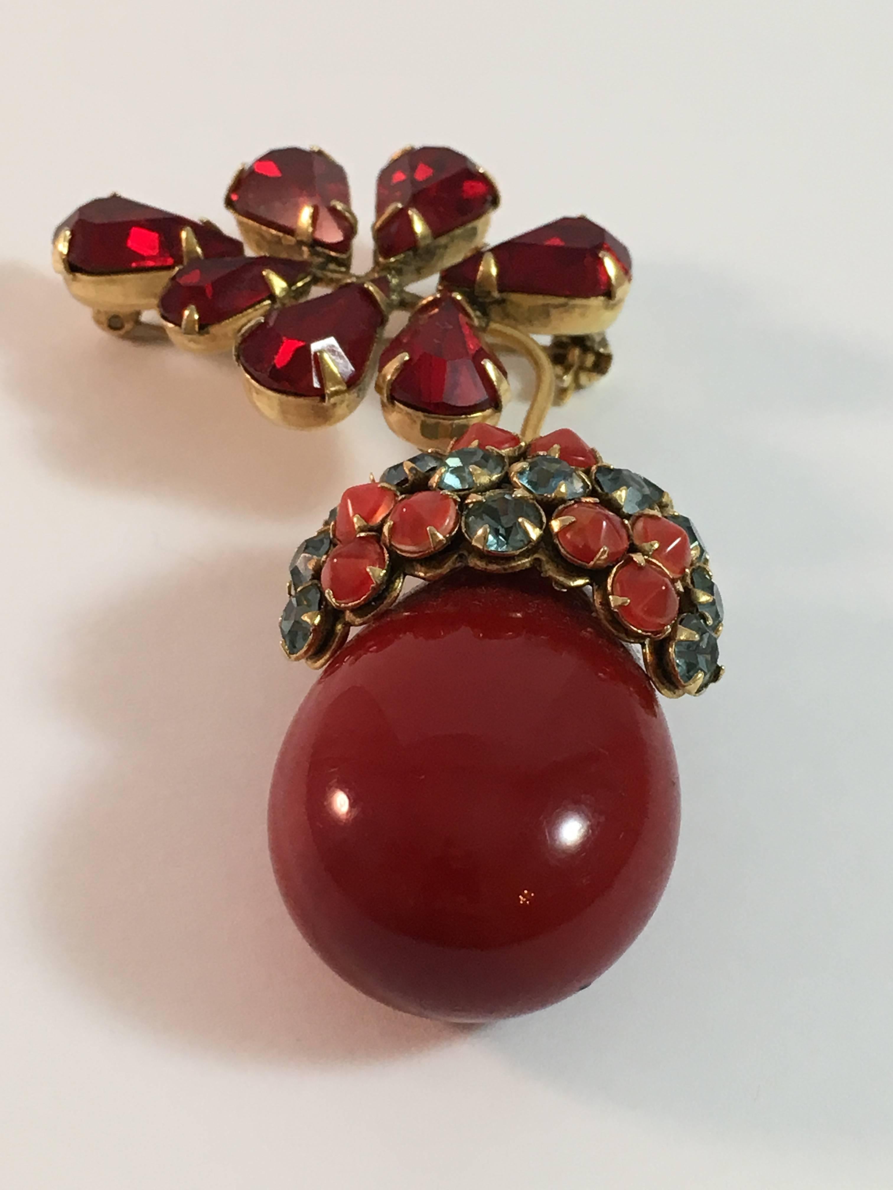 This is a 1950s Schreiner New York red acorn brooch. It measures 2 1/2" long x 1 1/2" at its widest point. The red acorn portion is made out of a resin. The acorn's cap features red and blue crystals set with the stones pointing out