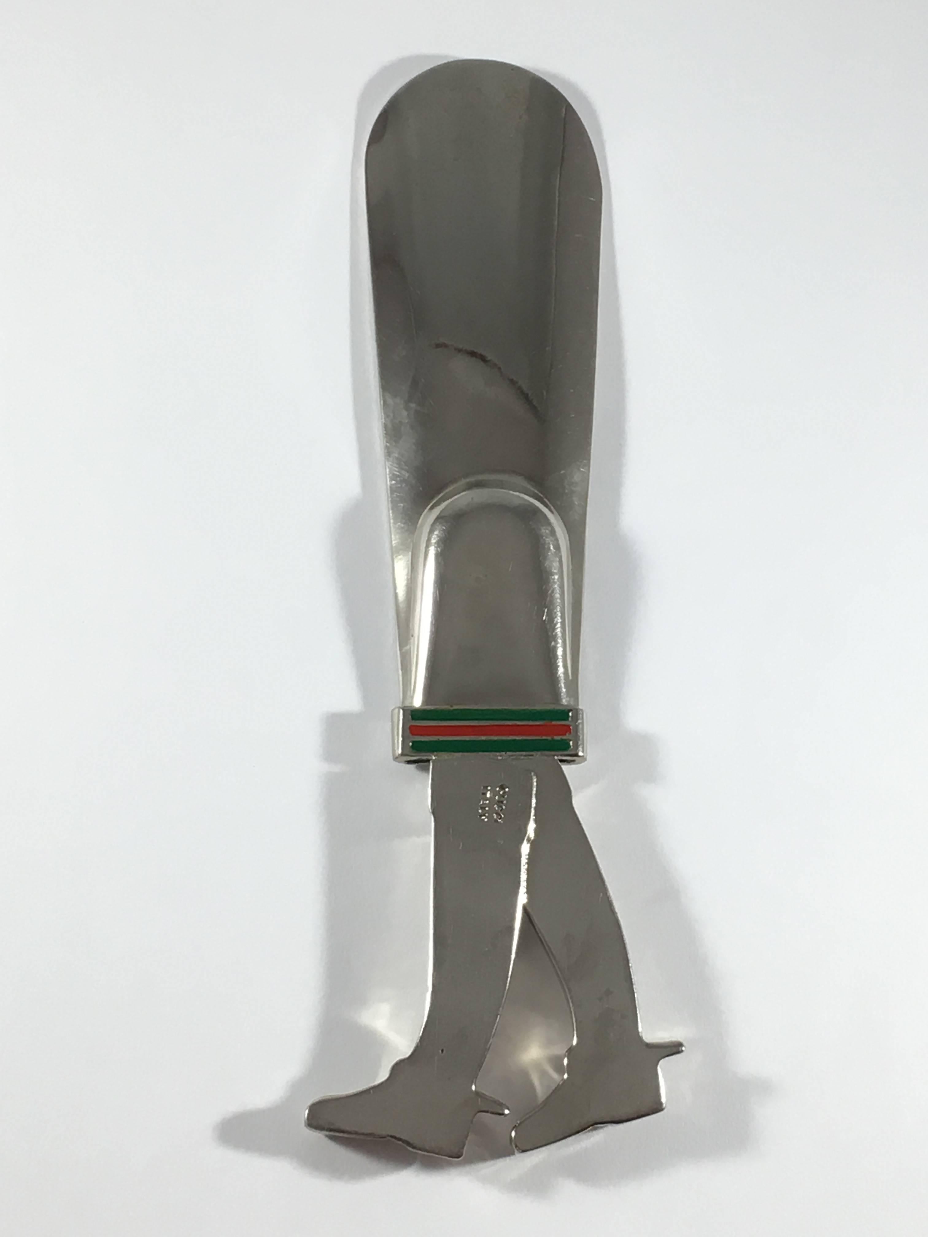 This is a 1970s Gucci shoe horn with equestrian boots and red and green enamel stripes. It is made out of silver-tone metal and features equestrian boots and red and green enamel stripes. It is in very good condition with slight wear to the finish