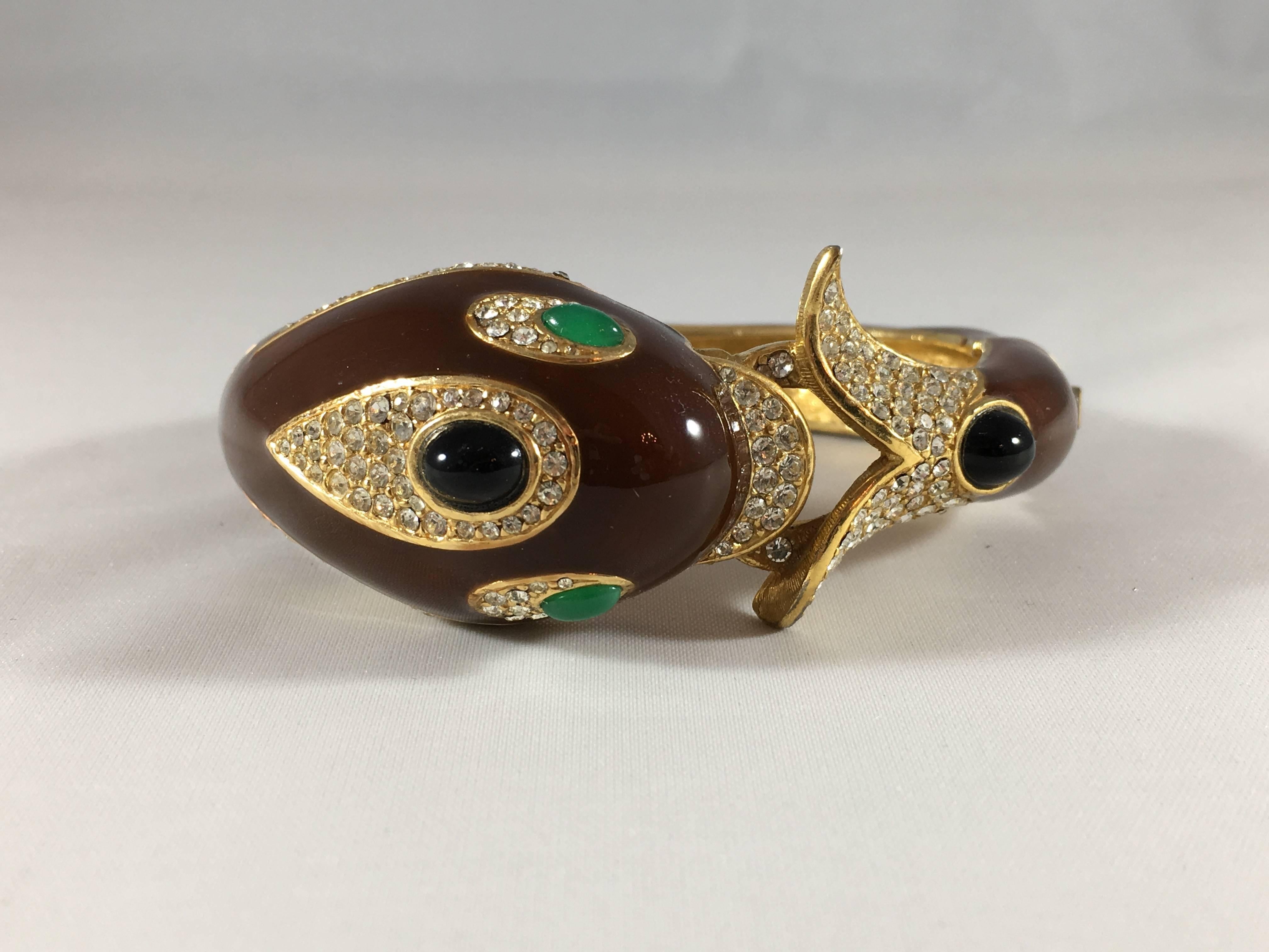 This is a 1970s brown enamel and crystal Ciner dolphin bracelet. It has green glass eyes and measures 1