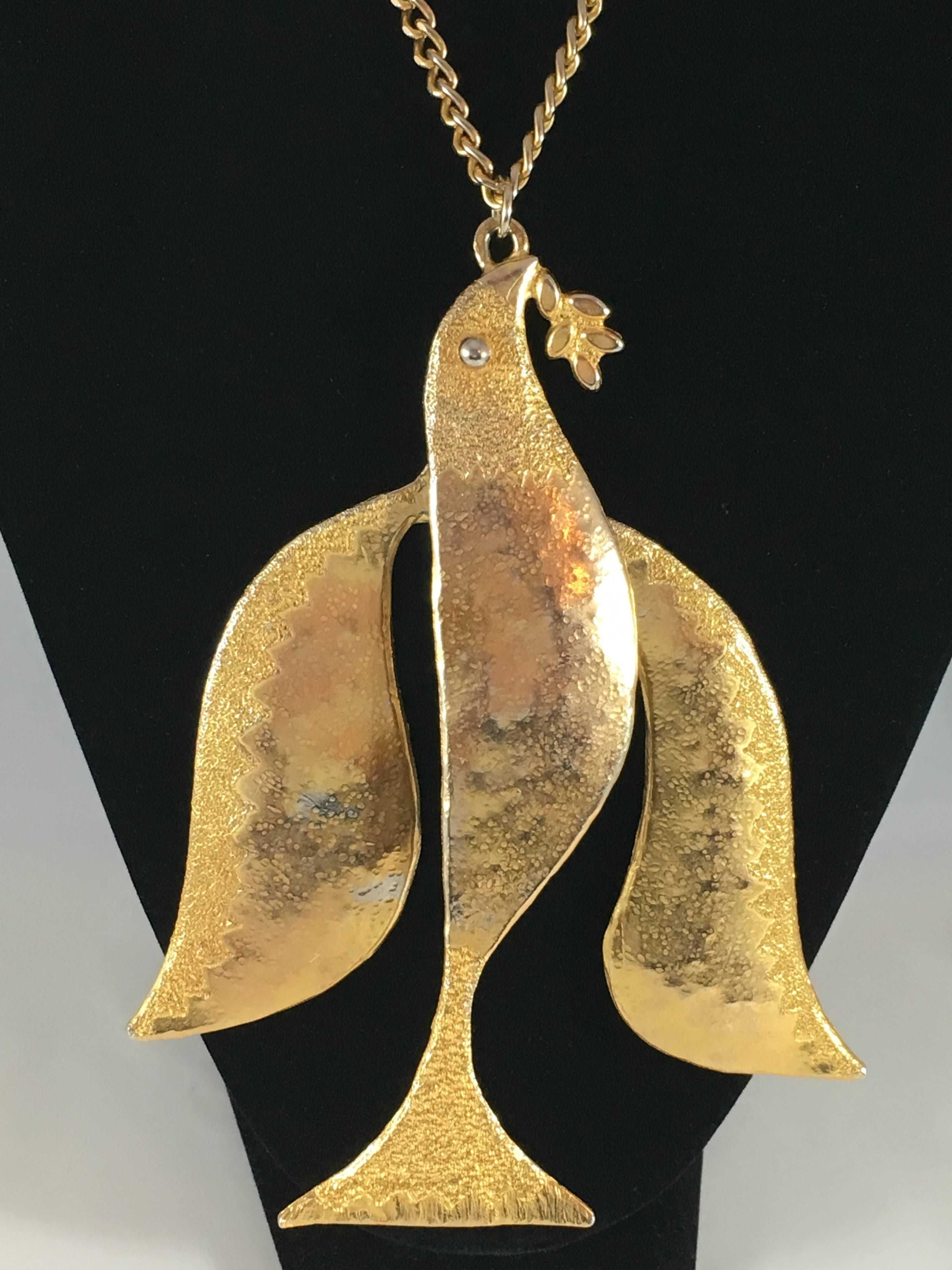 This is a rare 1970s dove pendant necklace from Kenneth Jay Lane. The pendant is huge. It measures 6 3/8 inches long and features a dove holding an olive branch in its mouth. The widest part measures 5 1/2 inches. It is made up of three articulated