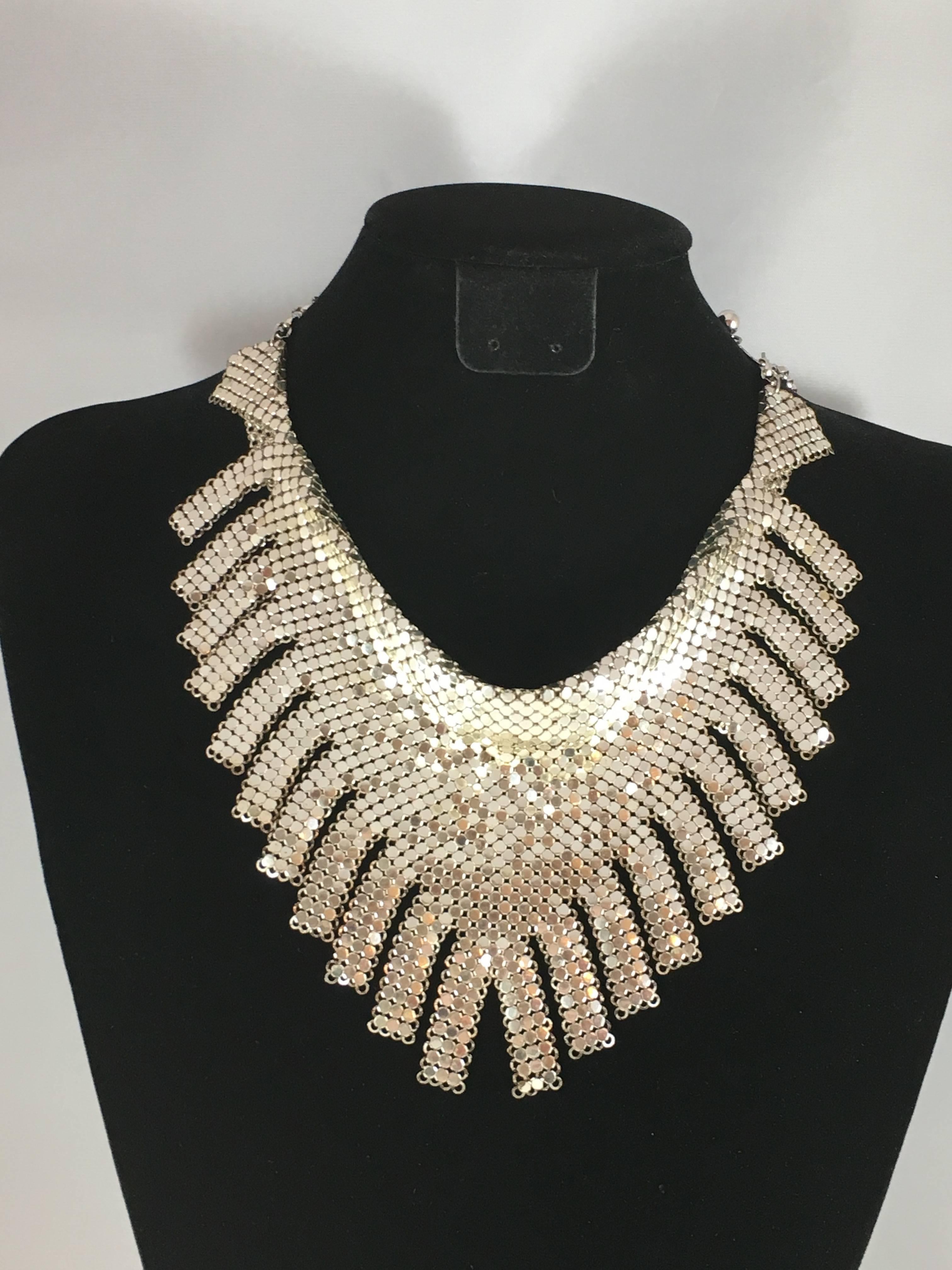 This is a 1970s silver-tone bib necklace with fringe from Whiting and Davis. It is made out of Whiting and Davis' famous chainmail construction. The necklace measures 20 1/2" long and is adjustable. It can be worn as a choker or a little