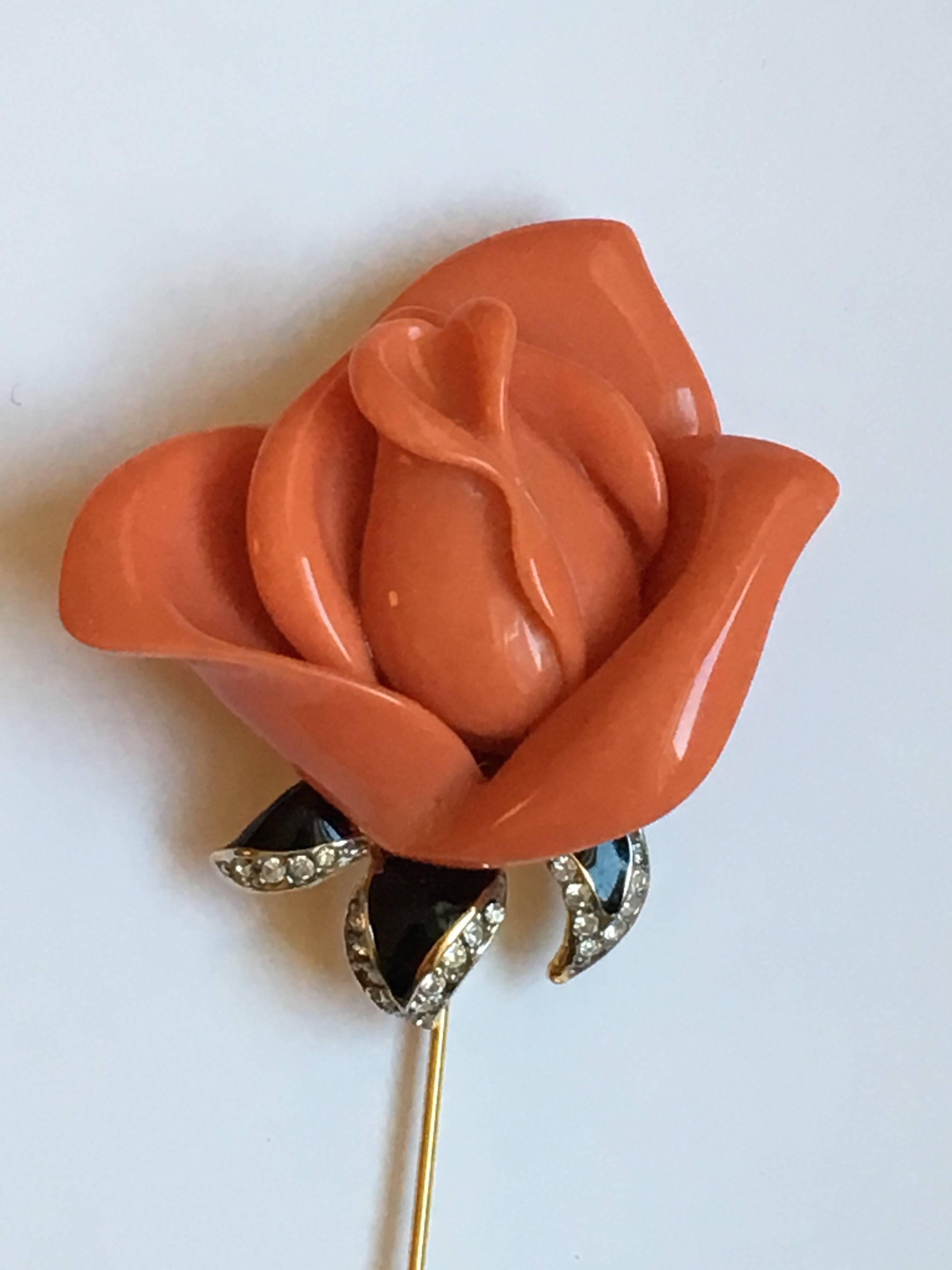 This is a great stick pin from Kenneth Jay Lane. The rose is made out of a coral colored resin. The rose's leaves are a black enamel highlighted with clear colored rhinestones. The back is marked 'Kenneth Lane' in an oval shaped plaque. It measures
