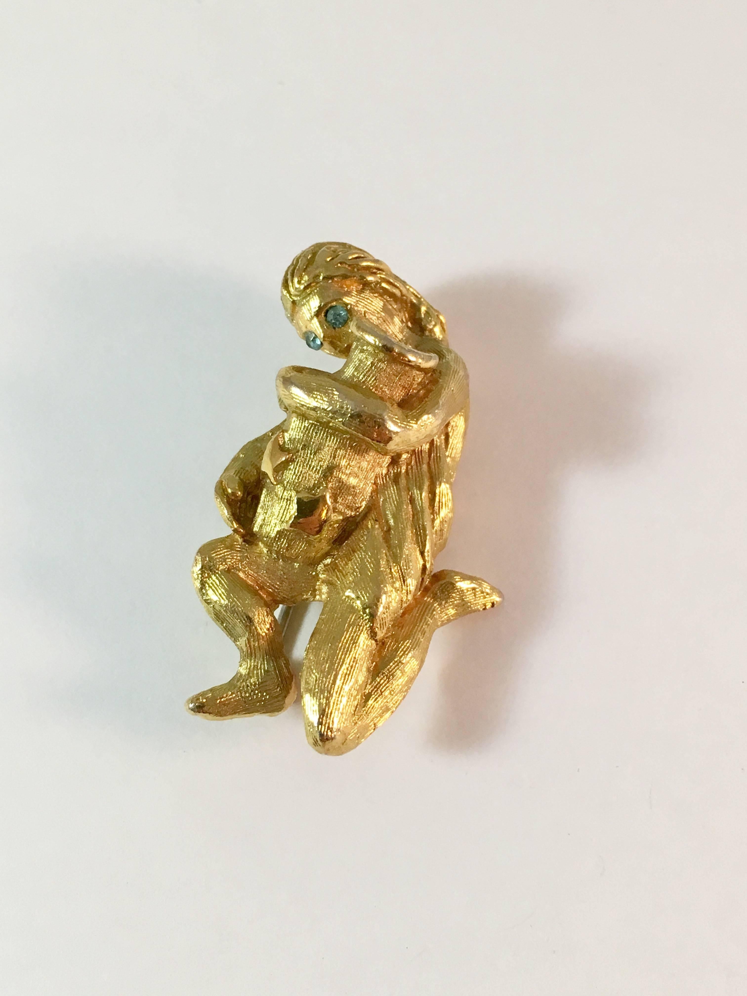 This is a gold-tone Kenneth Jay Lane Aquarius or Water Bearer brooch from the 1960s. It measures 1 1/2 inches long x 1 inch wide. The long haired robed figure has two aqua-blue rhinestone eyes. She is kneeling and holding an urn of water with stars