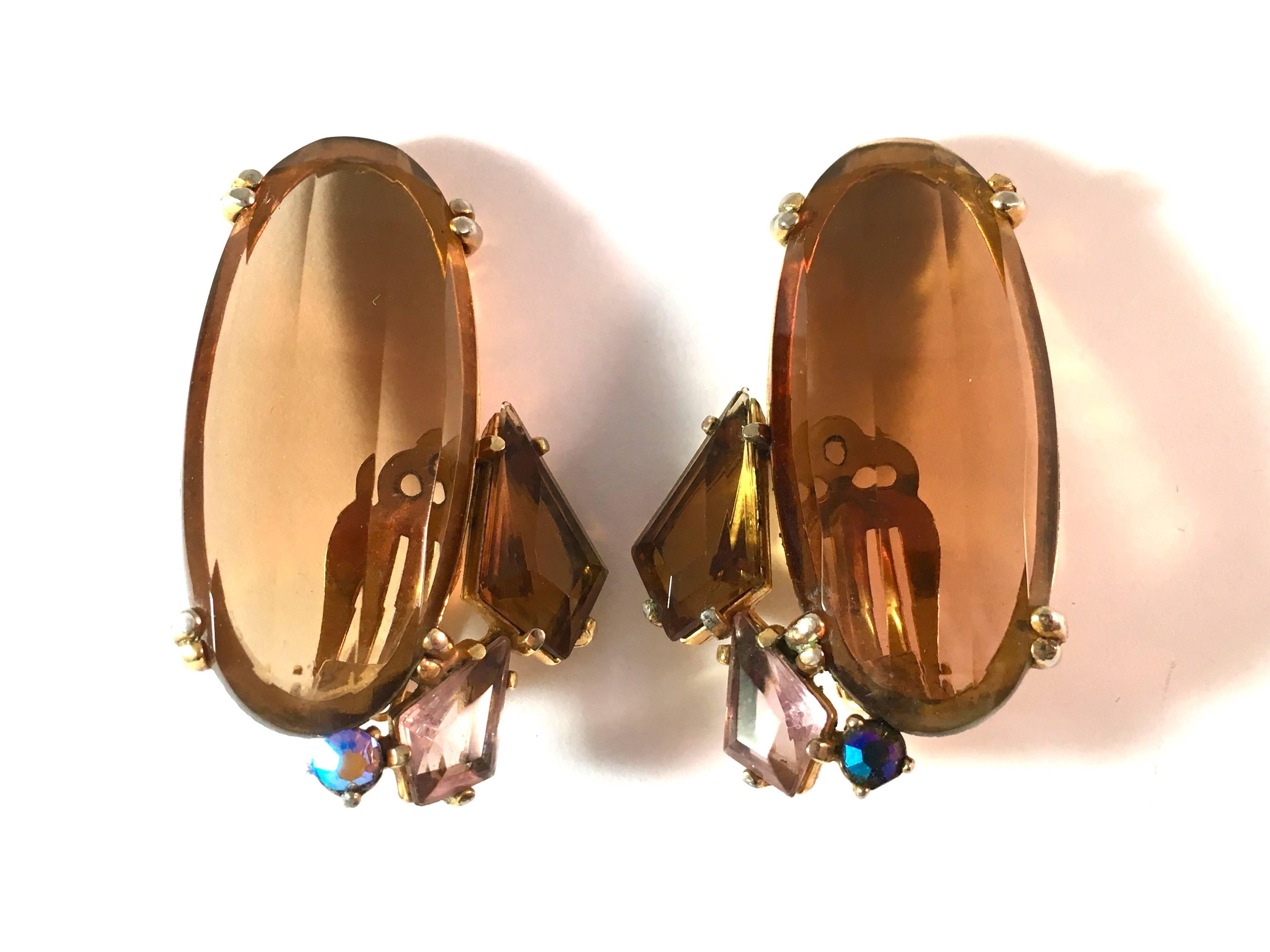 These huge Elsa Schiaparelli clip-on earrings are from the 1940s. Each earring is  made up of a large faceted light brown topaz glass stone set with two additional stones and an aurora borealis. The earrings have a gold-tone base metal. They are