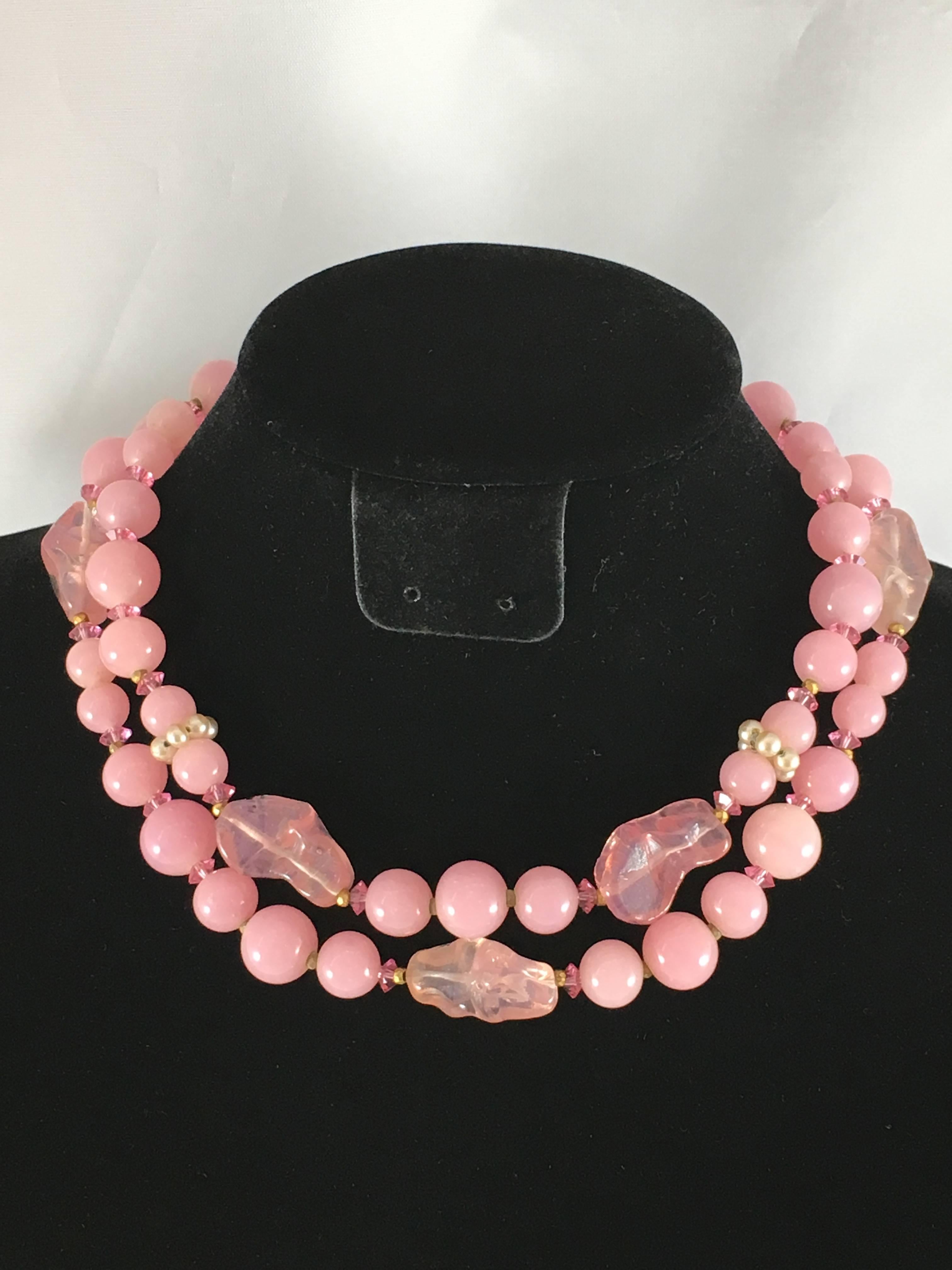 This is a beautiful 1950s two strand pink glass choker necklace made by Miriam Haskell. It features light pink glass beads, faceted dark pink glass beads and faux seed pearls. It has a flower clasp made up of a pink glass center and faux seed pearl