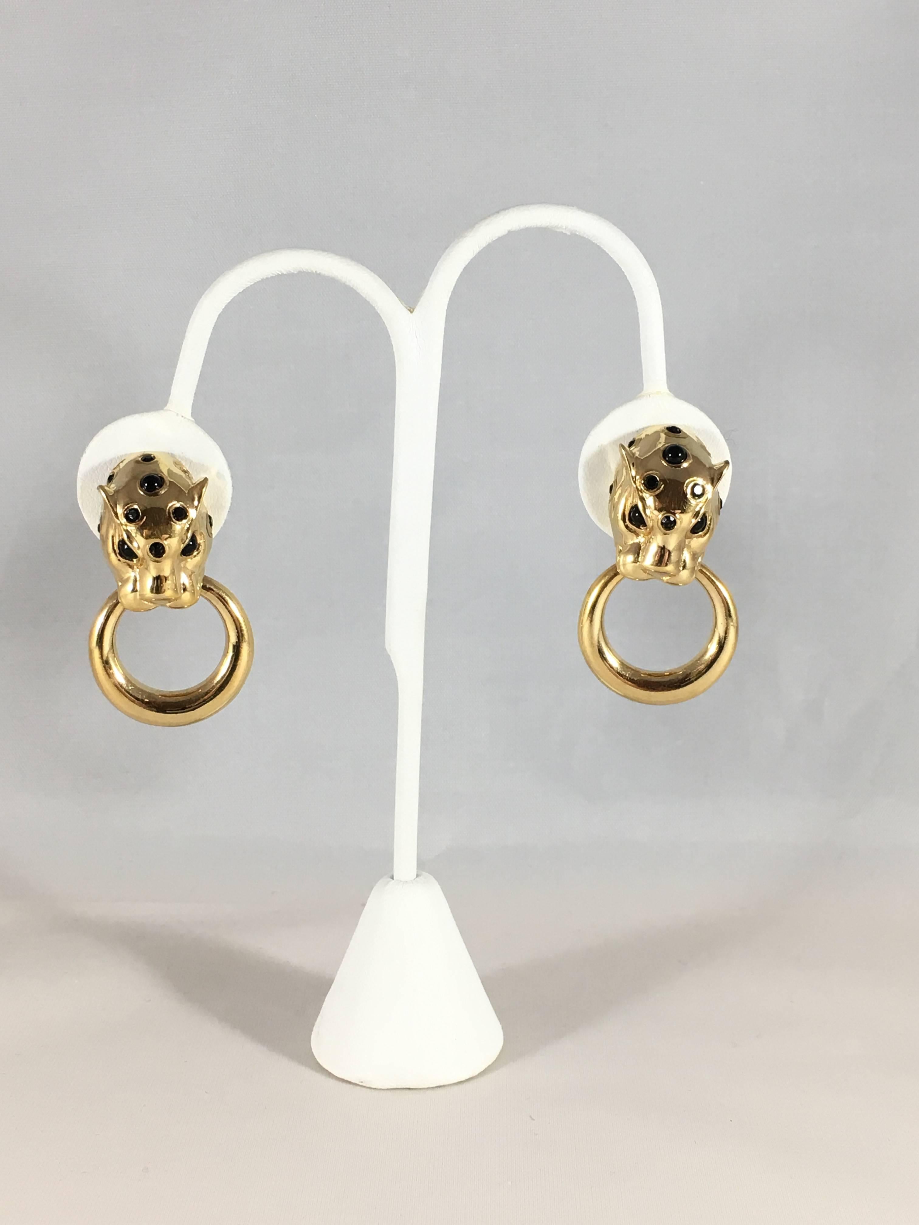 This is a pair of leopard or panther head door-knocker clip-on earrings. They are gold-tone with black glass eyes and spots. They are marked 'Ciner' on the back of the clips and are in excellent condition. They measure 1 1/2 inches long and 1 inch