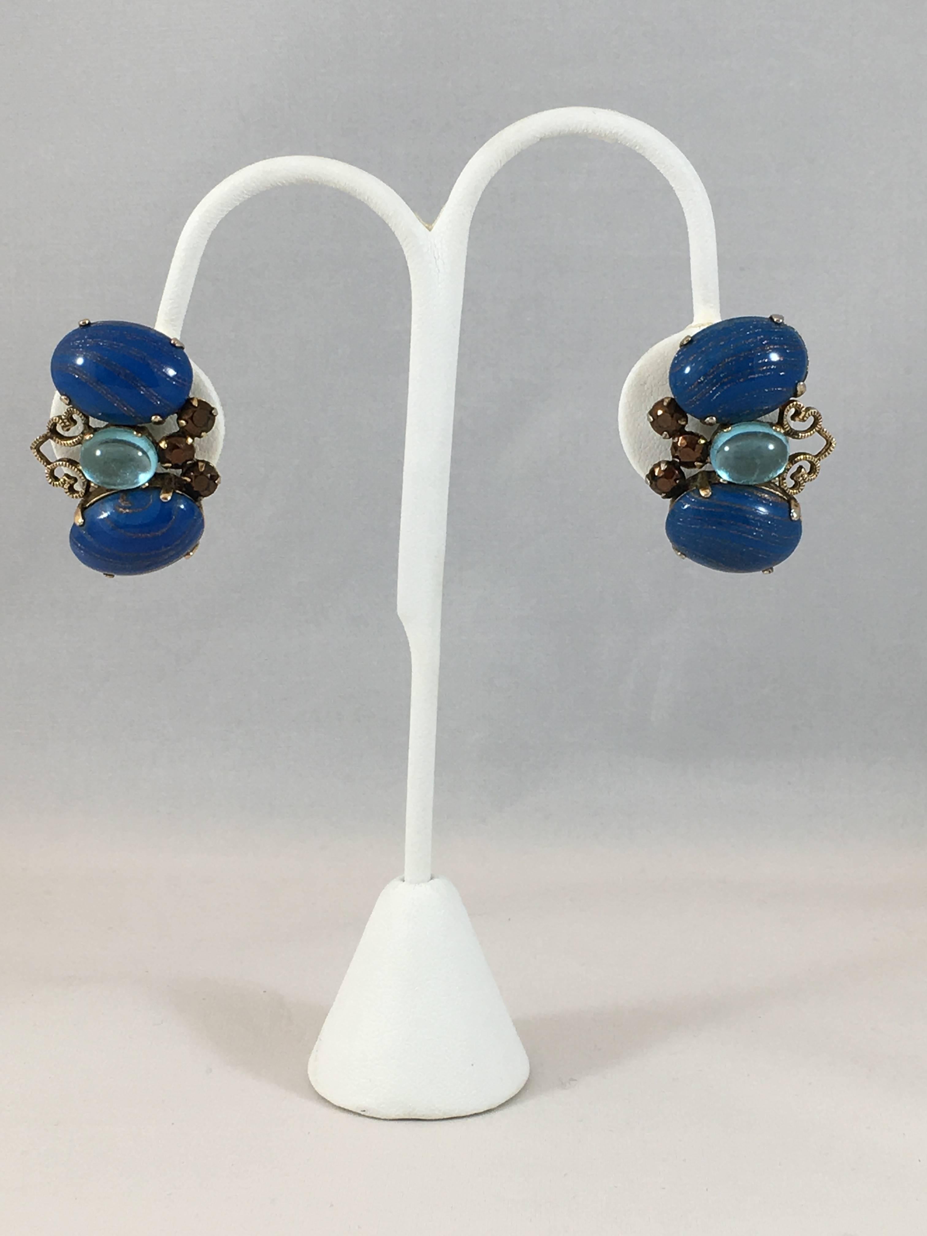 This is a beautiful pair of blue 1960s Schreiner clip-on earrings. They look as if they could be butterflies. They are made out of gold-toned metal set with beautiful blue and brown stones. The smaller brown stones are set with the pointed side up -