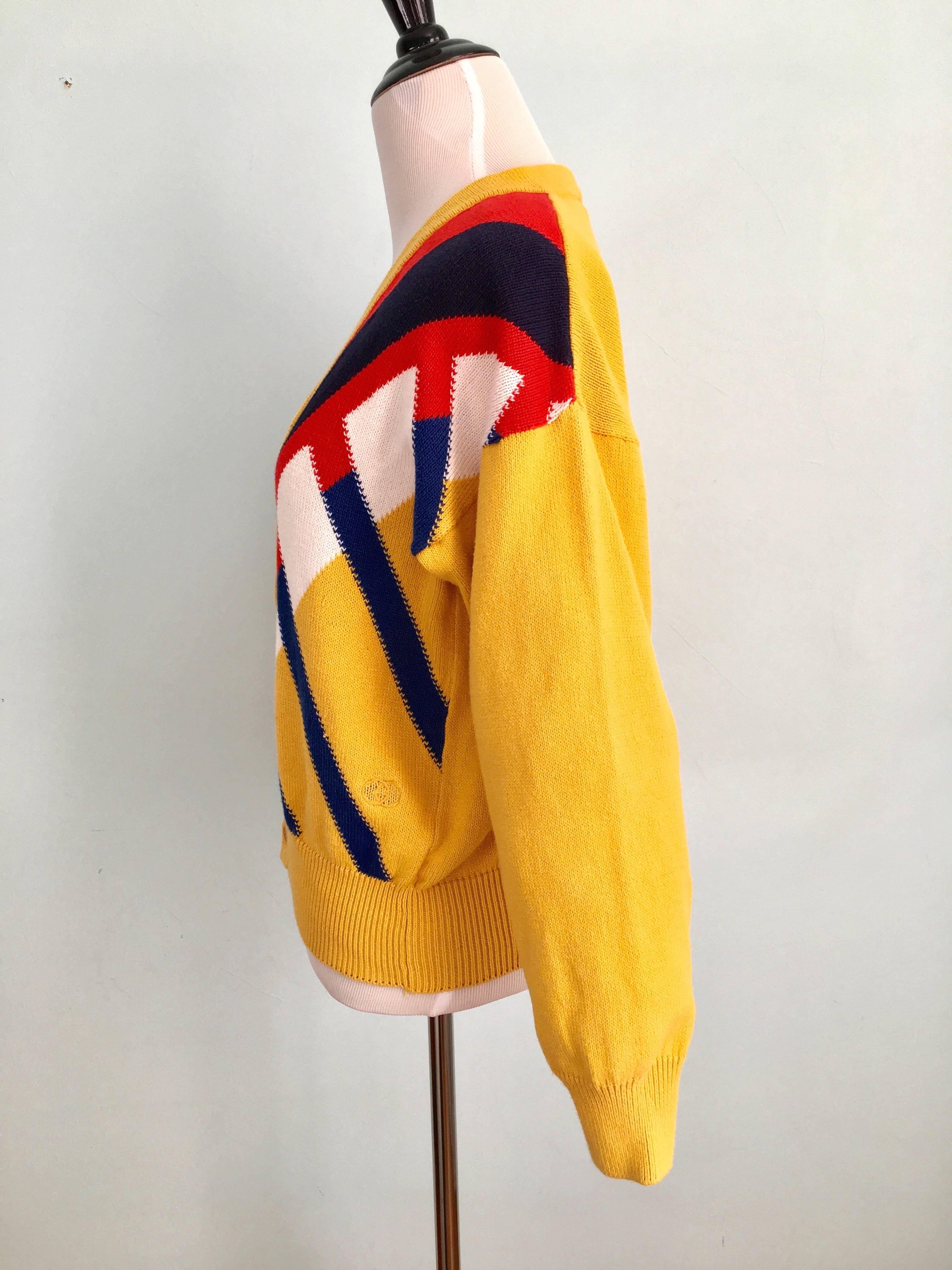 This is a 1980s cotton Gucci cardigan v-neck sweater with a graphic design on the front. On the front lower left side there is a yellow embroidered double "G" Gucci logo. The sweater is in excellent condition with the exception of a black