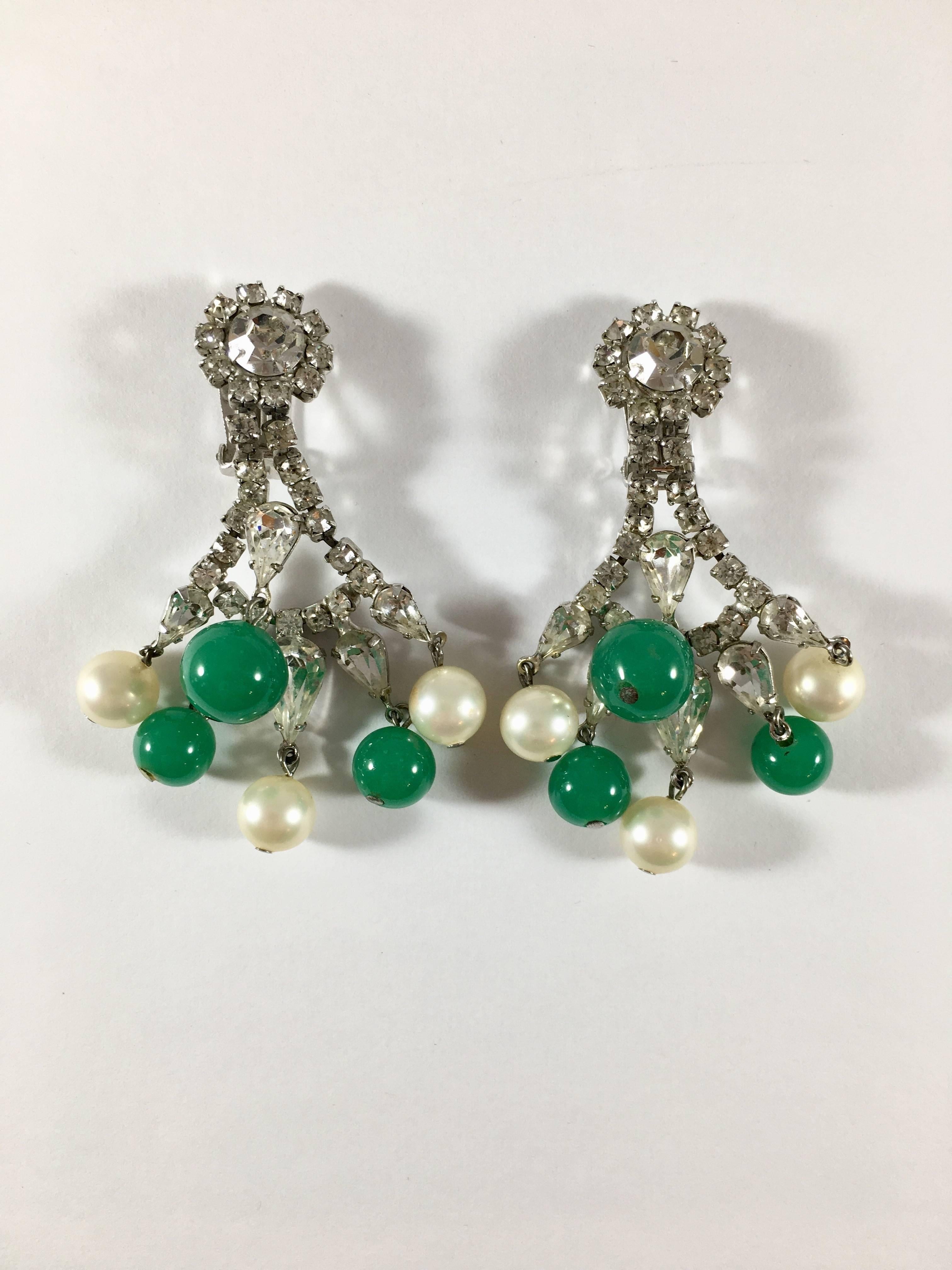 These beautiful 1960s chandelier dangle earrings from Hattie Carnegie are perfect for the holidays. Sparkly and festive, they feature clear rhinestones, faux pearls and emerald green colored glass balls. They are clip-ons and are marked CARNEGIE on