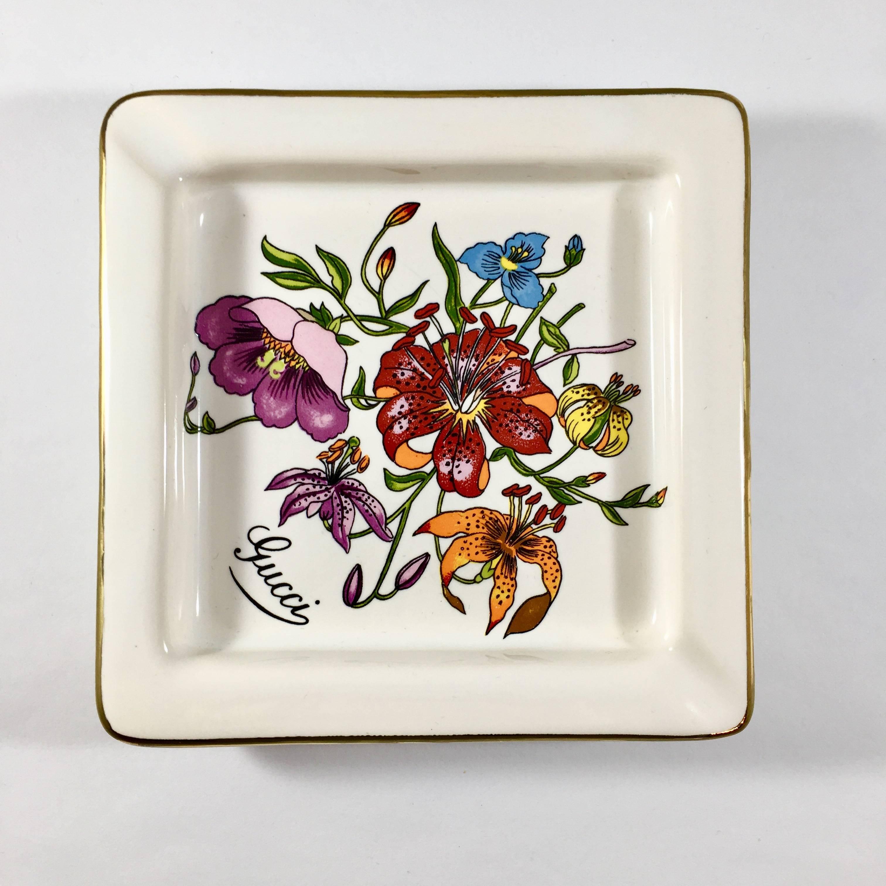 This is a vintage 1970s Gucci ashtray which can also be used as a jewelry or trinket dish. It is printed with the signature Gucci Accornero floral print and measures 5 inches x 5 inches square. It has a painted gold border around the edge and is