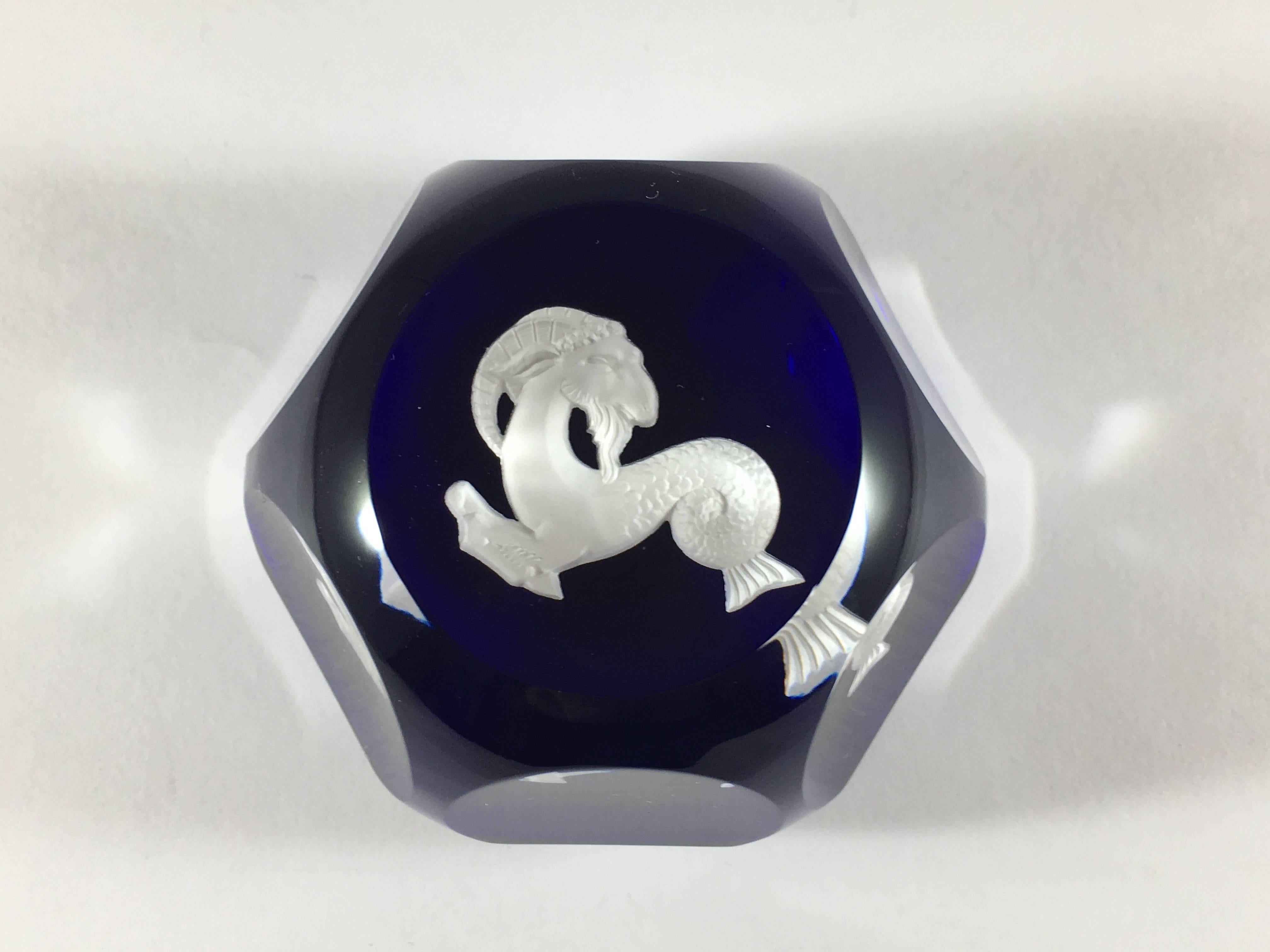 This is a 1970s cobalt blue and white sulphide Capricorn paperweight made by Baccarat. It has six faceted sides and measures 1 3/4 inches high and has a diameter of 2 1/2 inches. The bottom is etched with the Baccarat logo.  It is in excellent