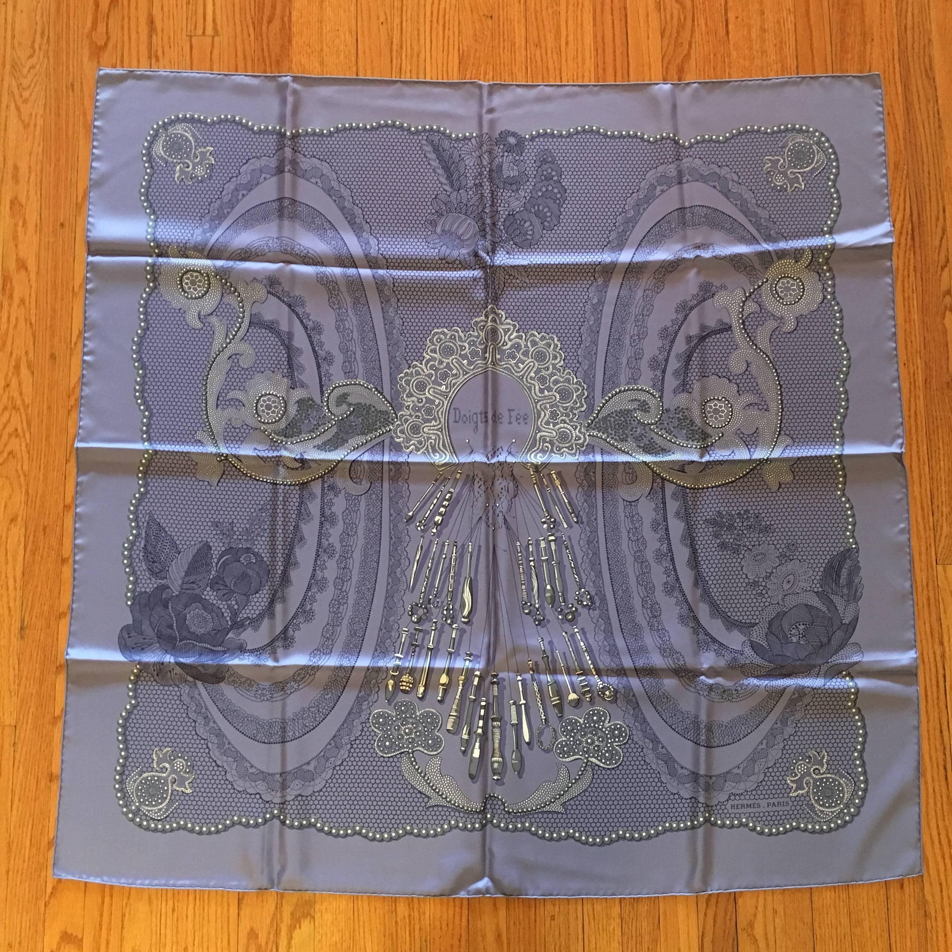 This is a beautiful periwinkle blue Hermes scarf called 'Doigts de Fee' or Fairy Fingers. It pays homage to the art of lace making and was designed in 2000 by Cathy Latham. The design features beautiful lacework as well as lace making tools. It is