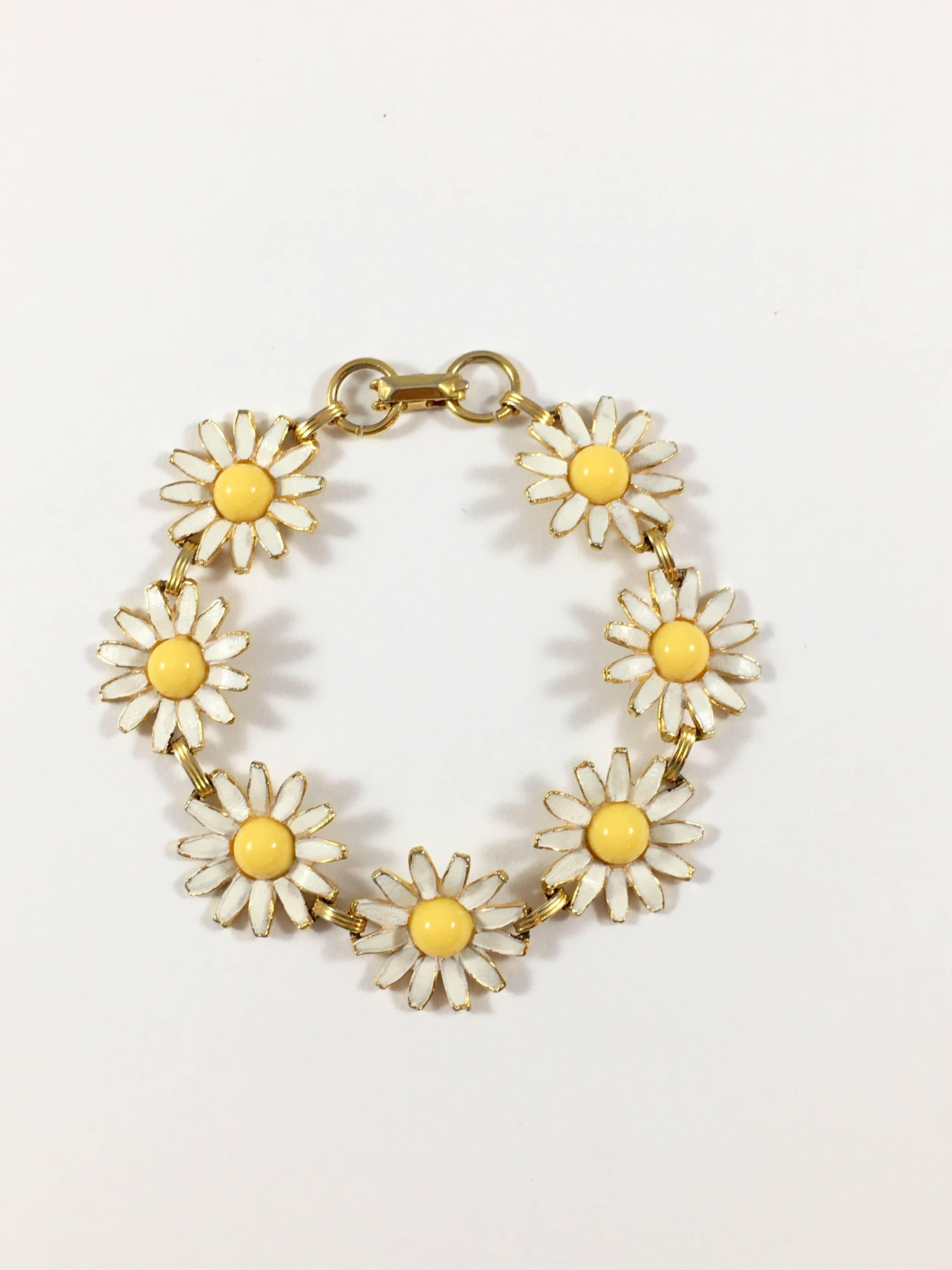 This is an adorable daisy bracelet from the 1960s. It is made out of a gold-toned material which has seven white enameled daisies with yellow resin centers. Each daisy is its own link. The bracelet is in excellent condition with only slight wear to