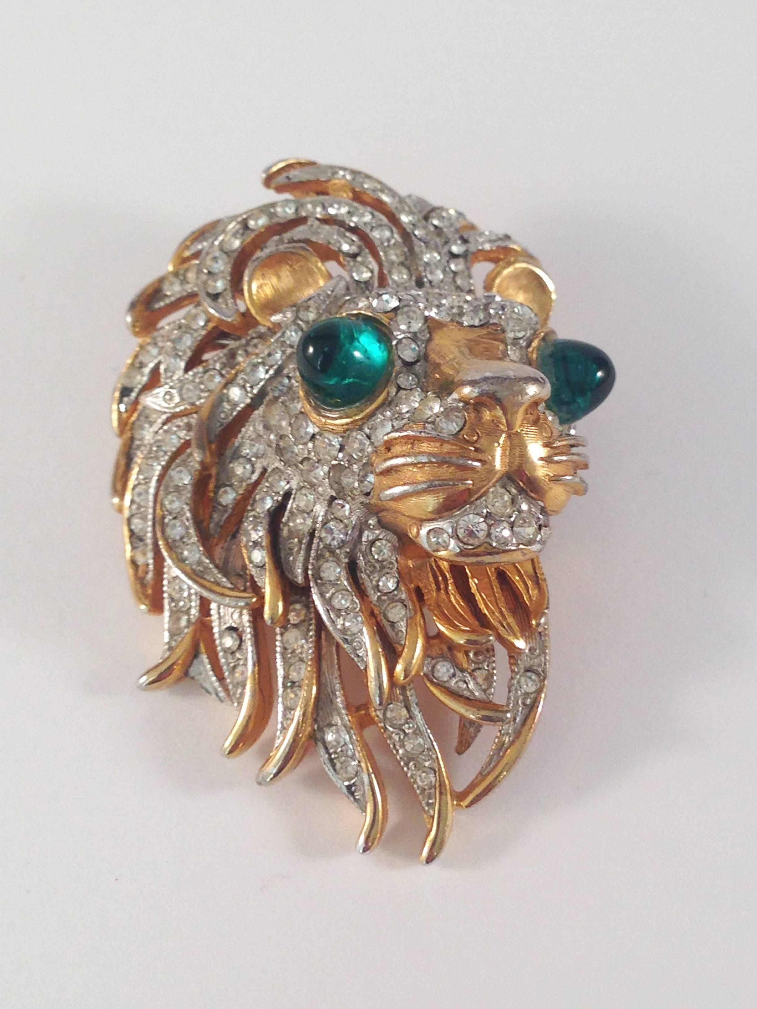 This is a beautifully made 1960s Kenneth Jay Lane brooch of a lion's head. It is gold-tone metal with clear rhinestones set into the mane and face and green glass eyes. It is marked 'K.J.L.' on the back - the signature Lane used in the 1960s. It is