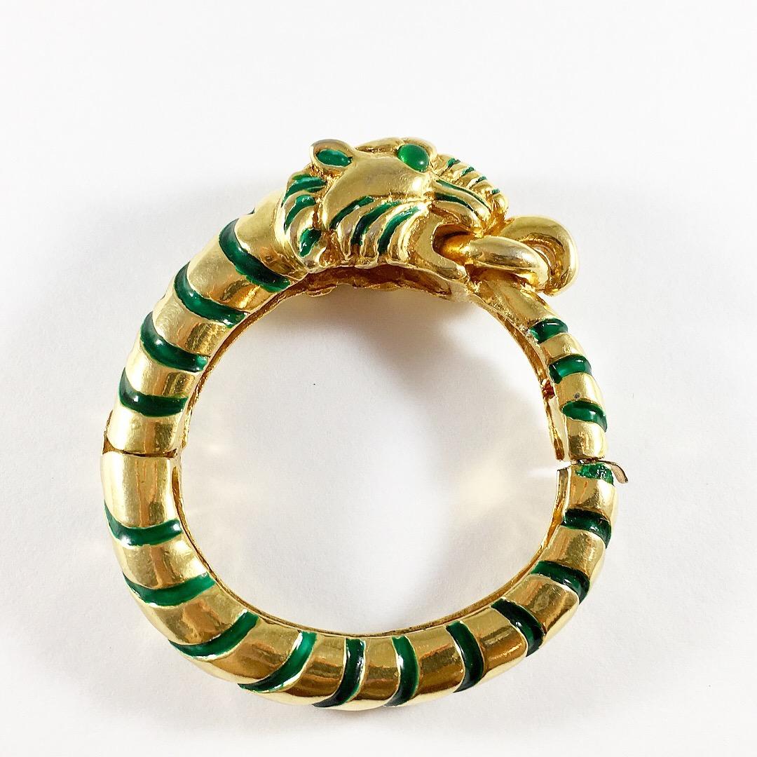 This is an amazing Kenneth Jay Lane tiger bracelet from the 1960s. It is beautifully made out of a gold-toned metal with green enamel stripes and green glass cabochons for the tiger's eyes. The bracelet would fit best on a small wrist. The interior