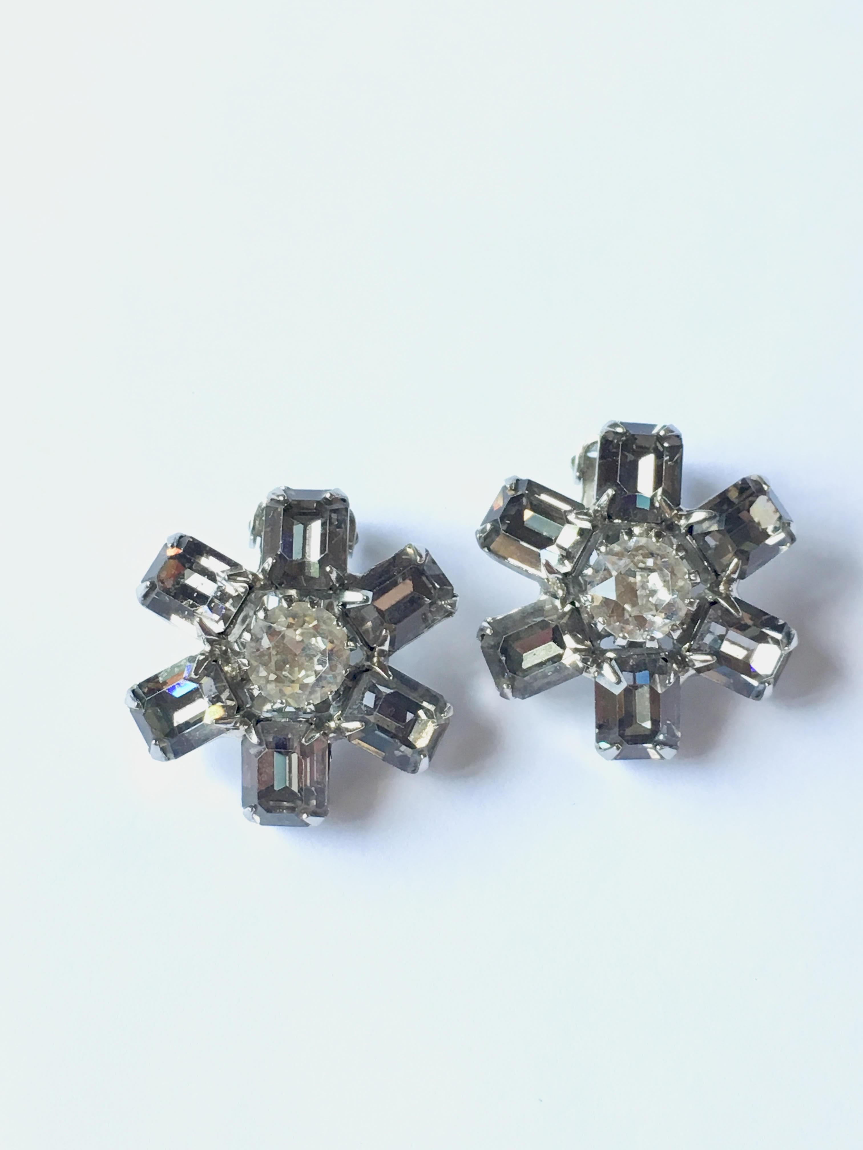 This is a beautiful pair of 1960s Weiss flower clip-on earrings. The petals of the flowers are light grey colored crystals and the centers of the flowers are a clear colored crystal. They are in excellent condition and marked 'Weiss' on the back of